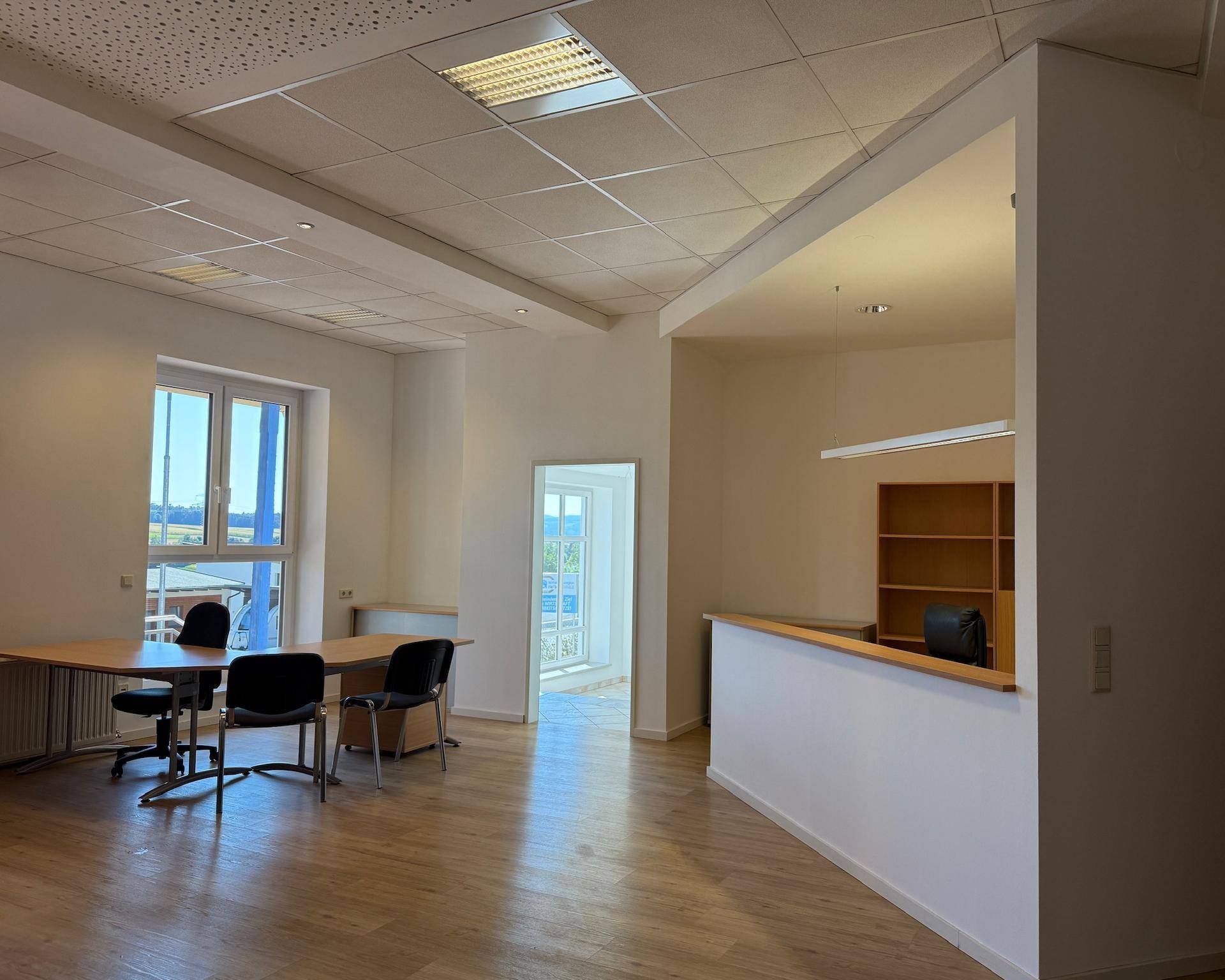 Heller Büroraum mit Laminatboden, großen Fenstern und einem Besprechungstisch, ideal für Arbeitsbereiche.