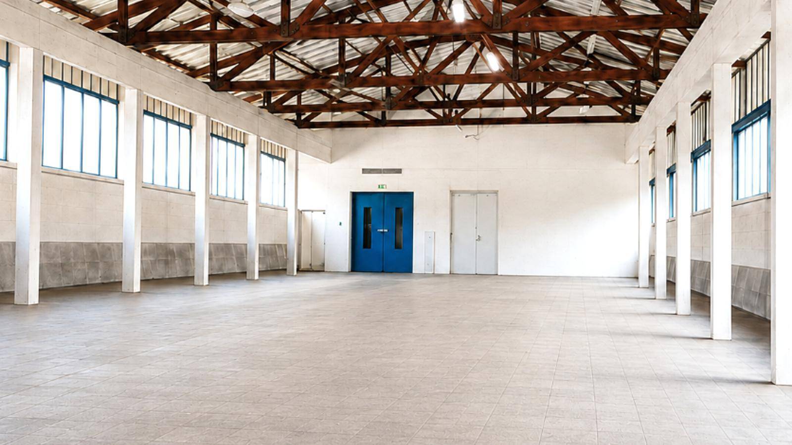 Geräumige Lagerhalle mit sichtbarer Dachkonstruktion aus Holz und viel Tageslicht durch große Fenster.