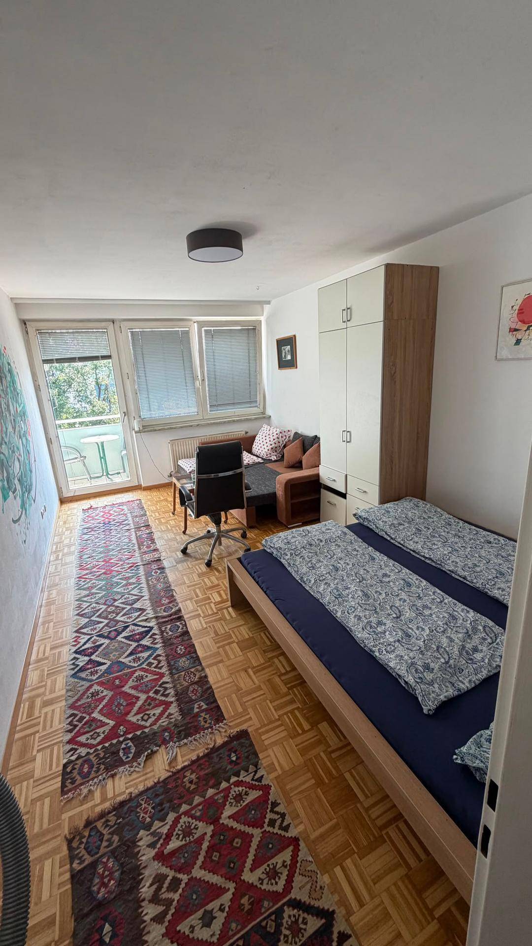 Helles Schlafzimmer mit Holzboden, Doppelbett, Kleiderschrank und Zugang zum Balkon.
