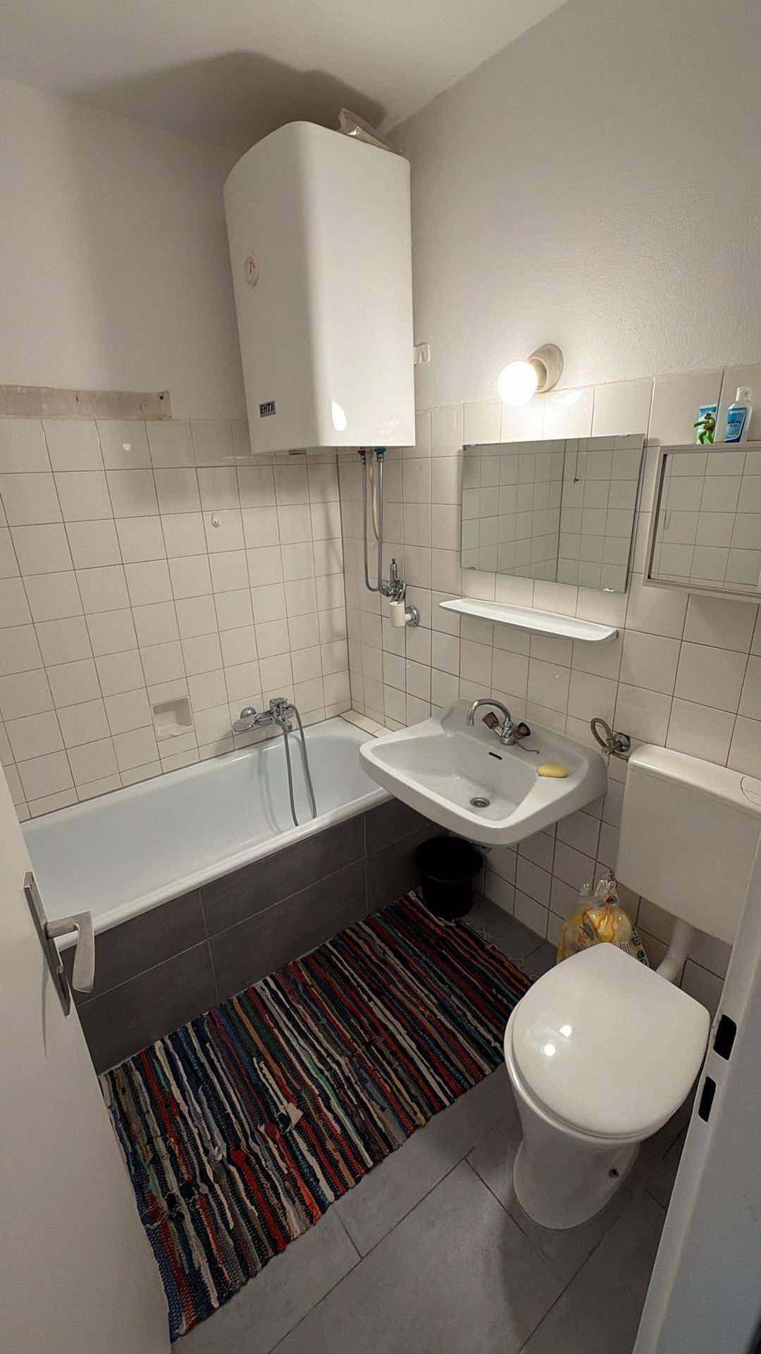 Funktionales Badezimmer mit Badewanne, Toilette, Waschbecken und weißen Wandfliesen.
