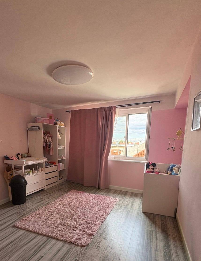 Kinderzimmer in Rosa mit Babybett, Wickelkommode und großem Fenster.