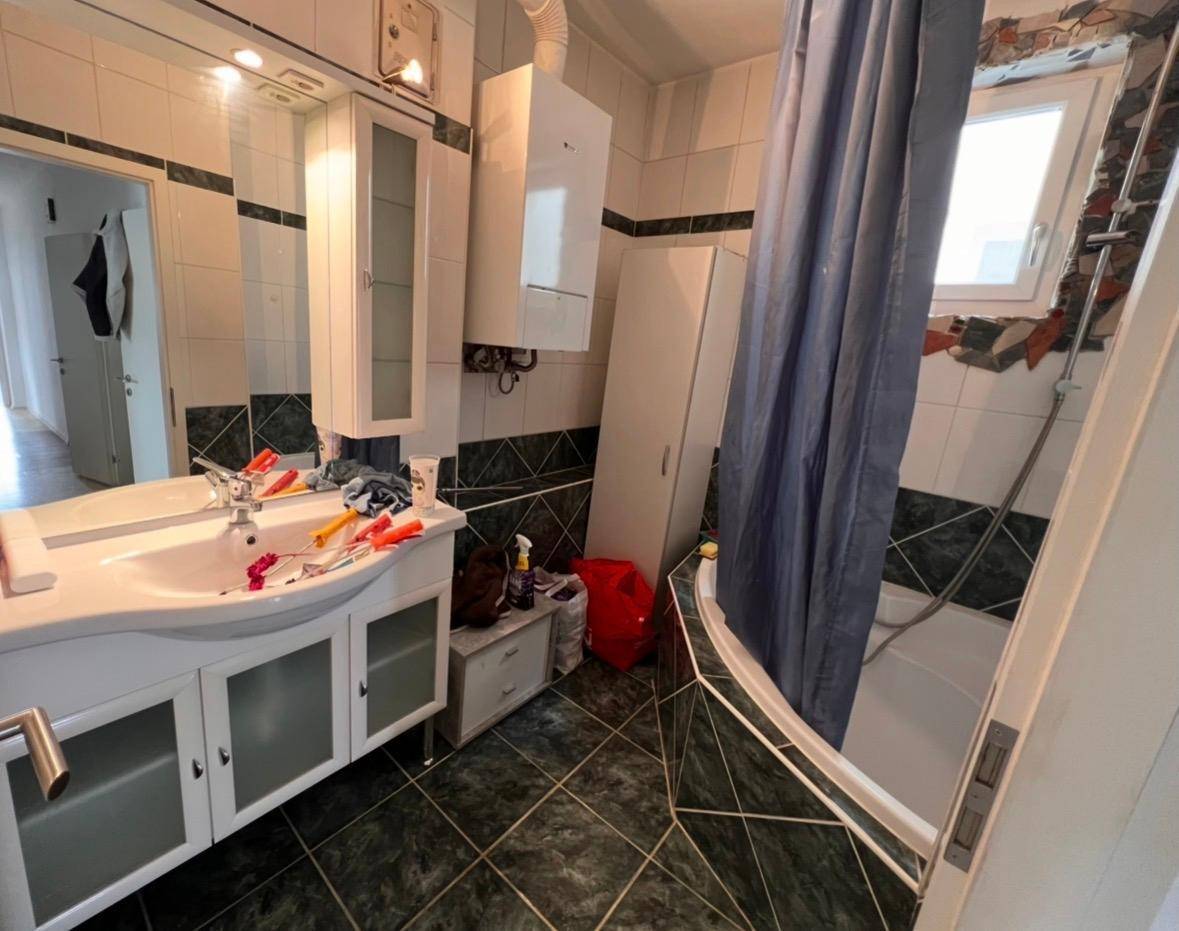 Badezimmer mit Badewanne, Waschbecken und Wandfliesen in Grün-Weiß.