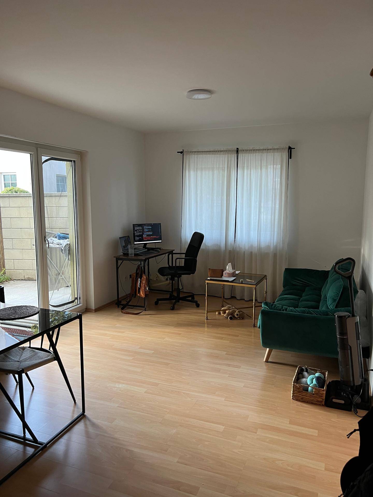 Helles Wohnzimmer mit Zugang zur Terrasse, Schreibtisch und einem modernen grünen Sofa.