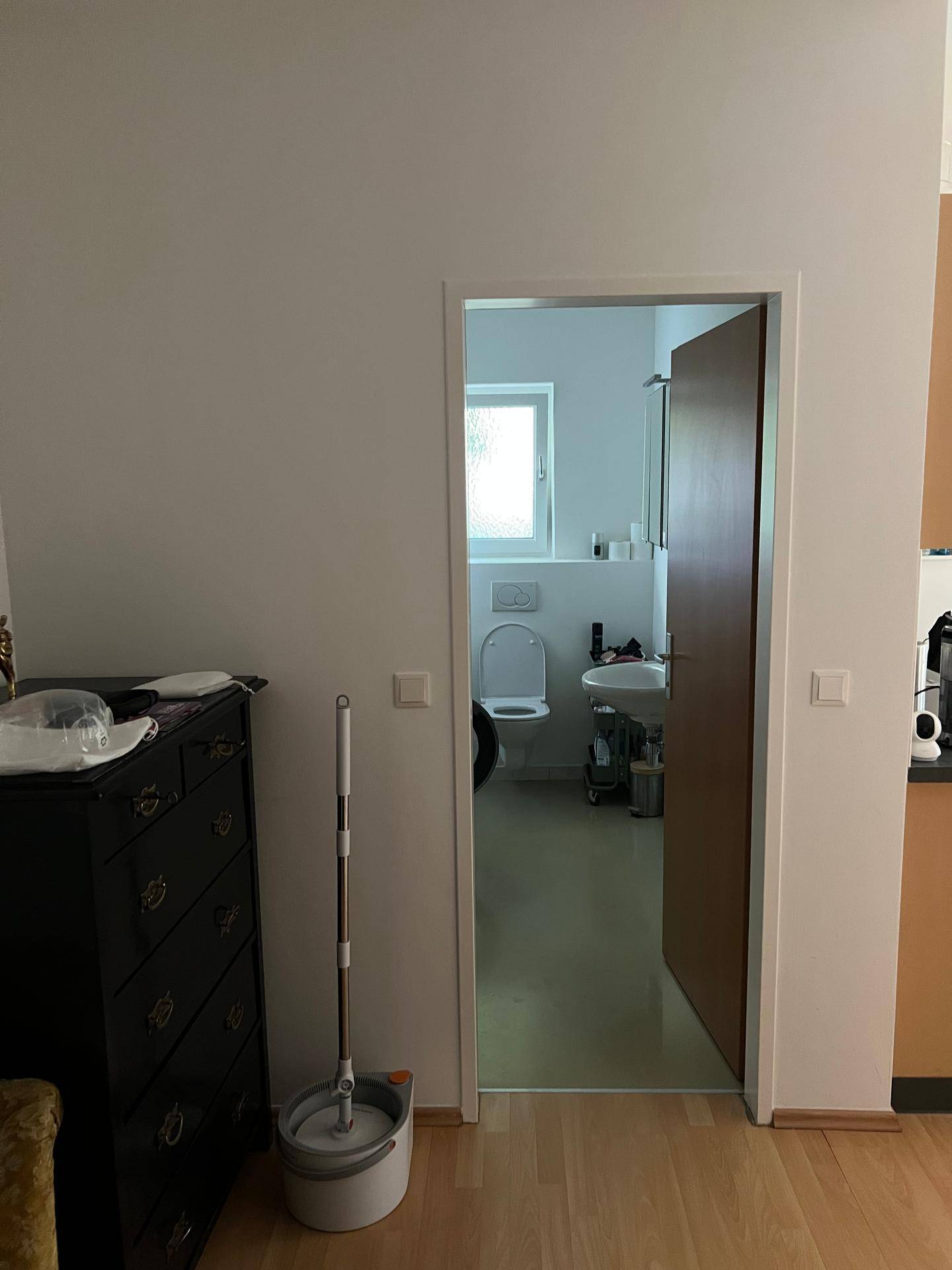 Blick von einem Wohnbereich in ein Badezimmer mit Toilette, Waschbecken und Fenster.