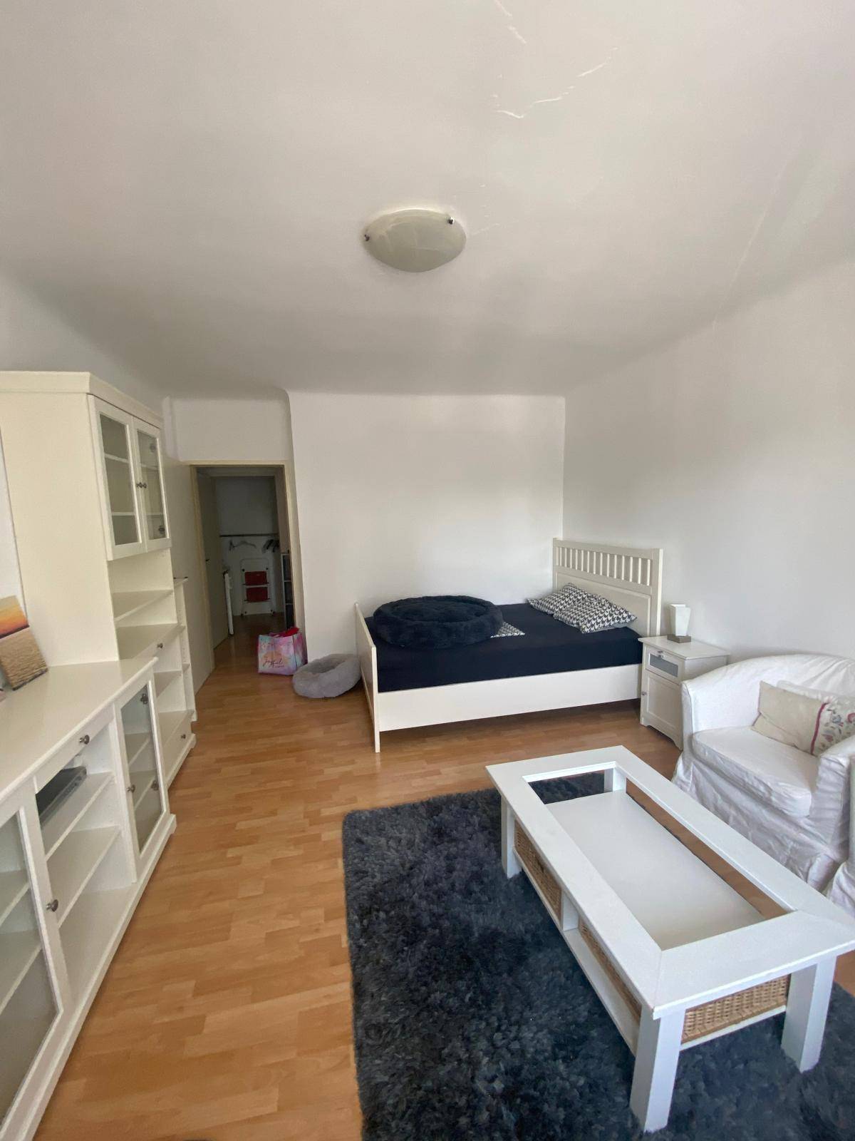 Kombiniertes Schlaf- und Wohnzimmer mit Bett, Couchtisch und weißen Schränken auf Holzboden.