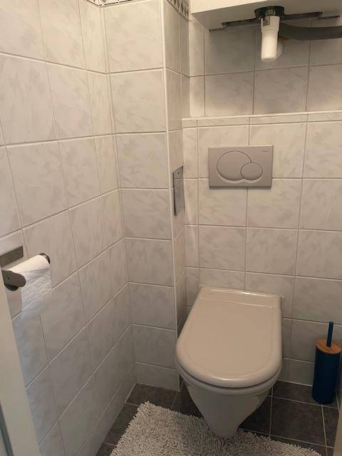 Kleines Gäste-WC mit wandhängender Toilette und hellen Fliesen an Wänden und Boden.