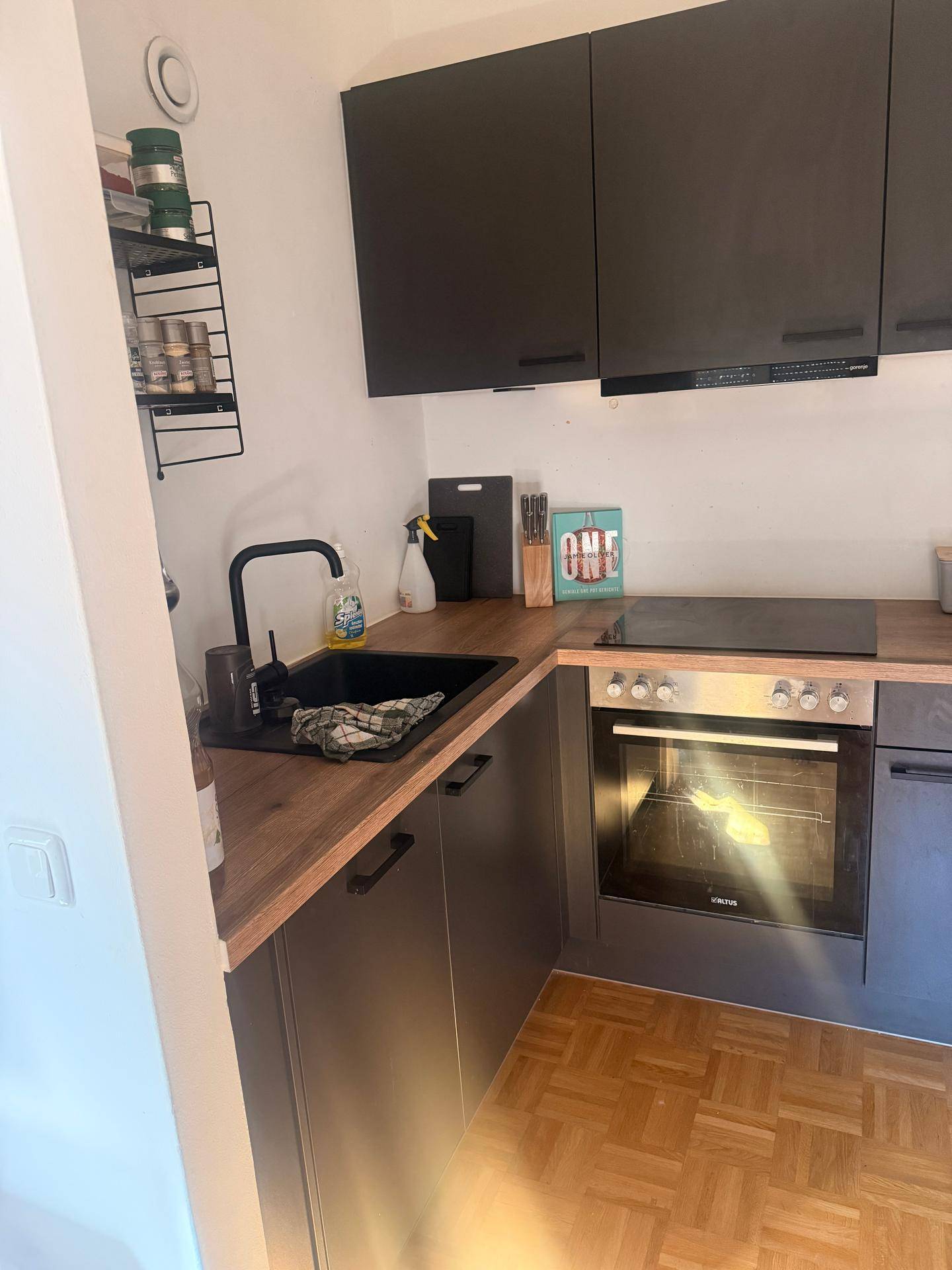 Moderne Küchenzeile mit dunklen Schränken, Holz-Arbeitsplatte und integriertem Backofen.