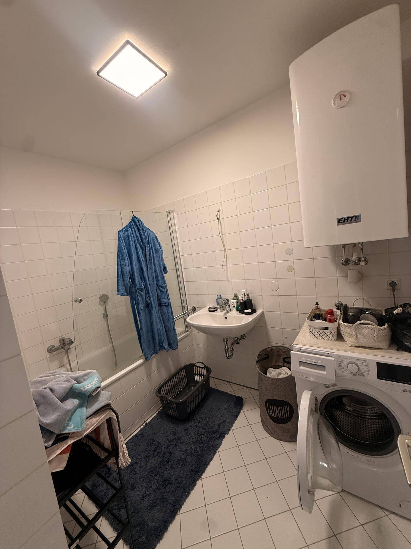 Funktionales Badezimmer mit Badewanne, Waschbecken, Waschmaschine und Boiler.