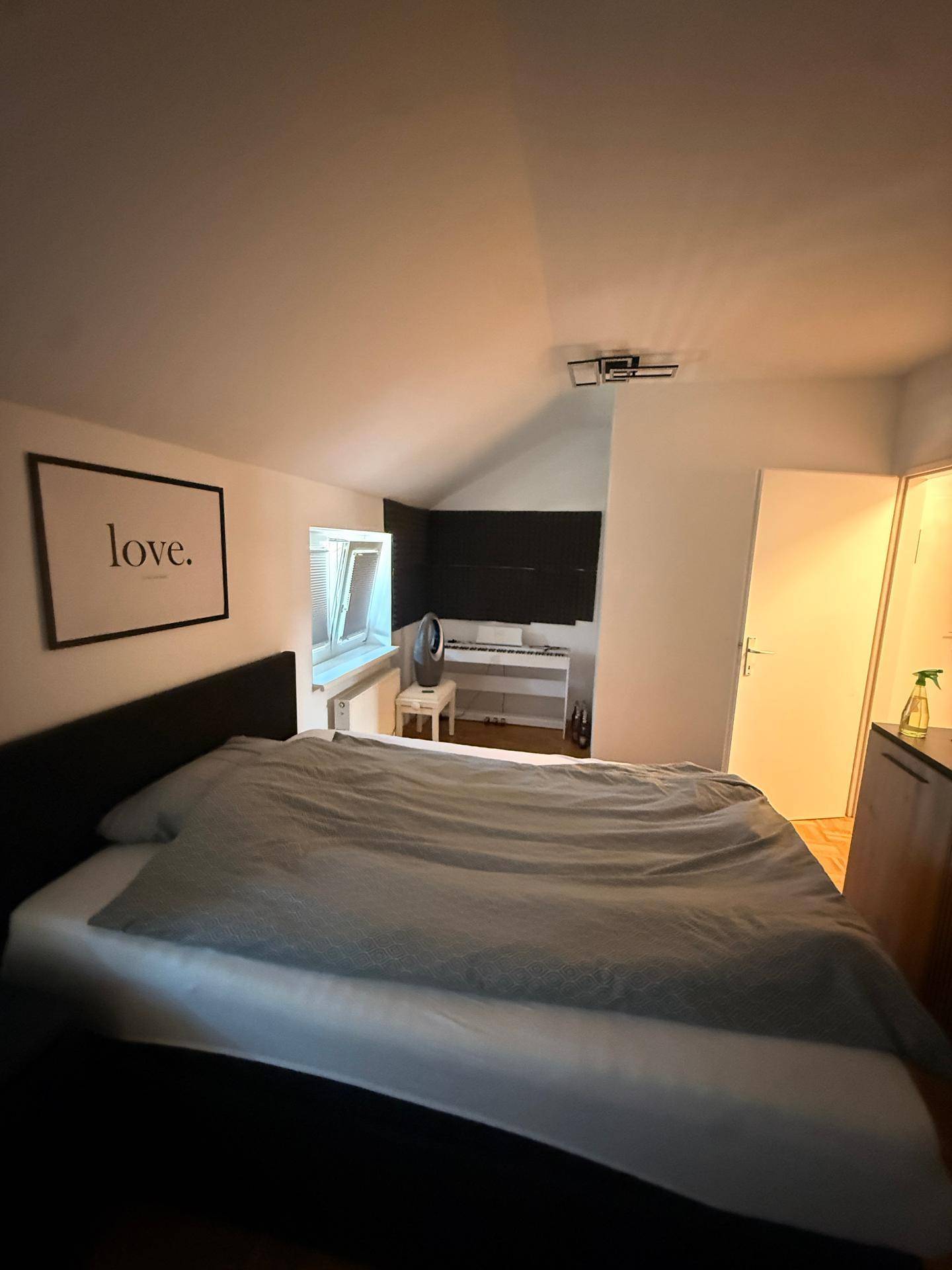 Helles Schlafzimmer mit Dachschräge, Doppelbett und Parkettboden.