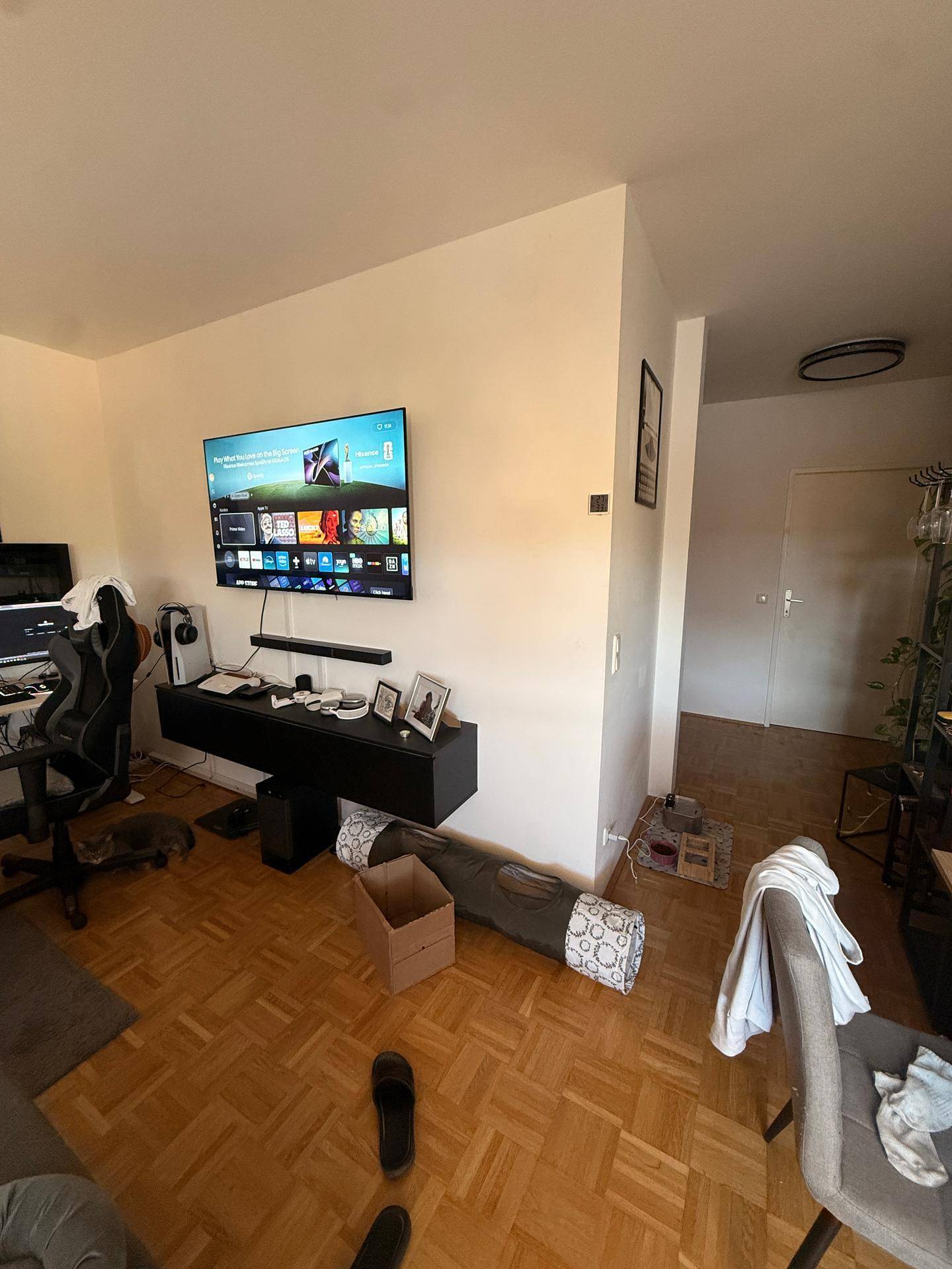 Heller Wohnbereich mit Wandfernseher, Schreibtisch und klassischem Parkettboden.