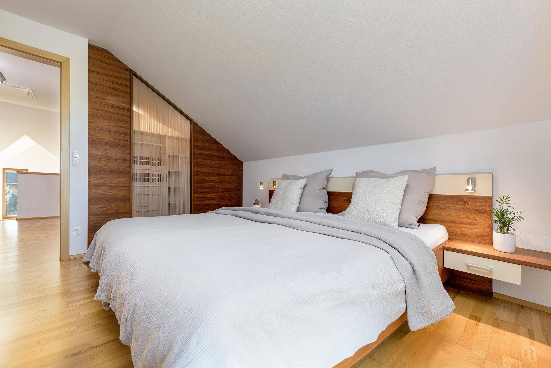 Schlafzimmer im Dachgeschoss mit Holzboden, Einbauschränken und schrägen Wänden.