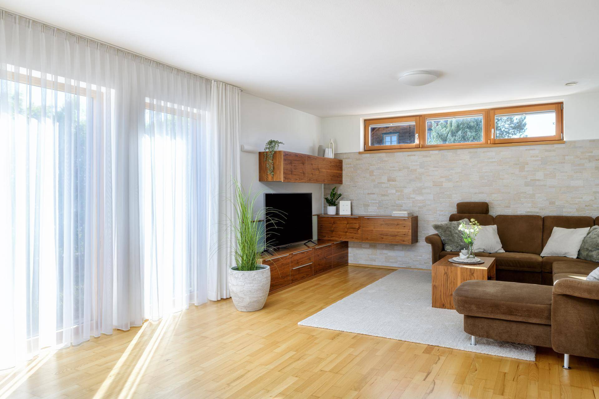 Lichtdurchflutetes Wohnzimmer mit großen Fenstern, Holzboden und modernem Mobiliar.