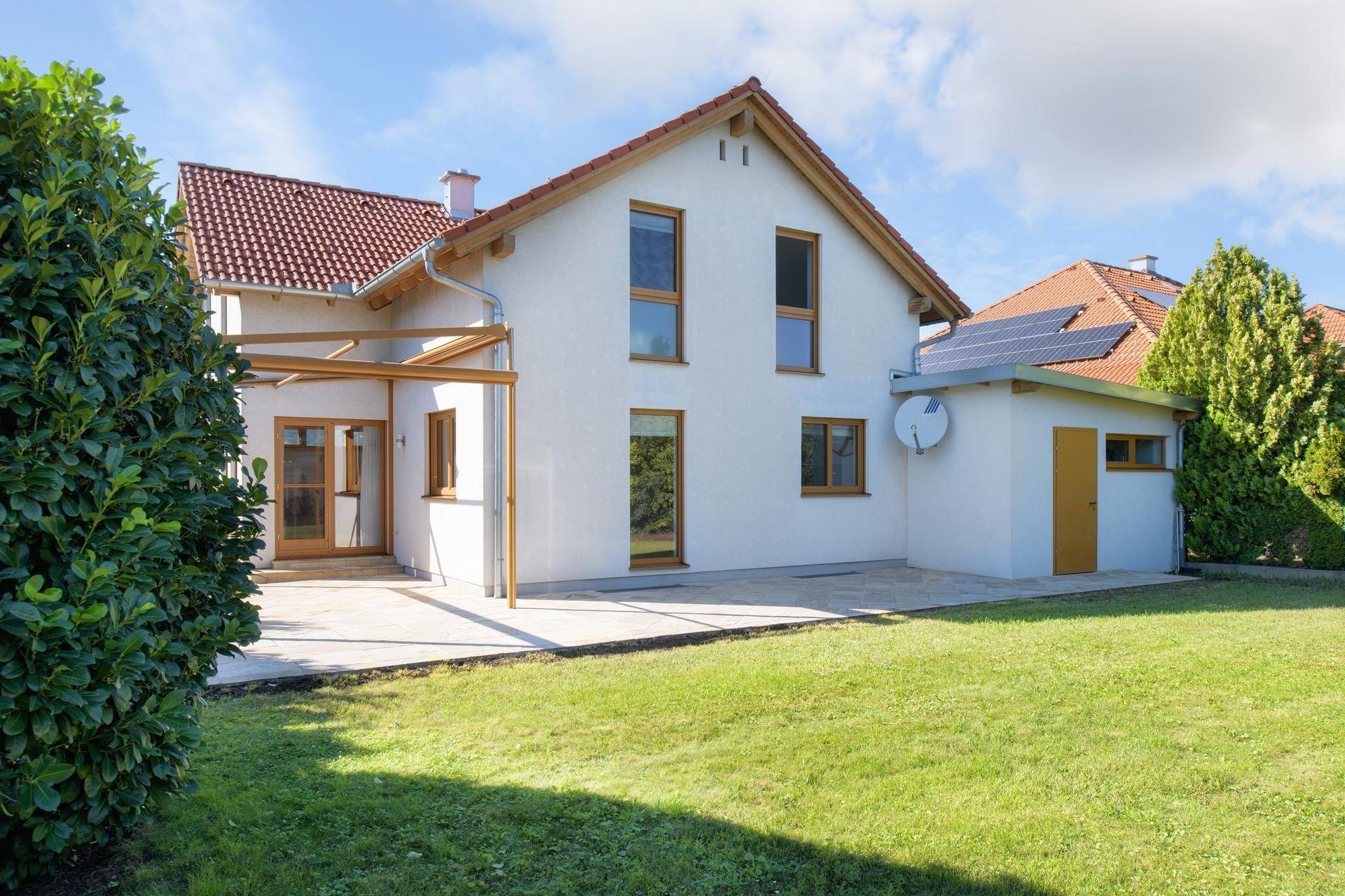 Hinteransicht eines modernen Einfamilienhauses mit großem Garten, Terrasse und einem Anbau mit Solaranlage.
