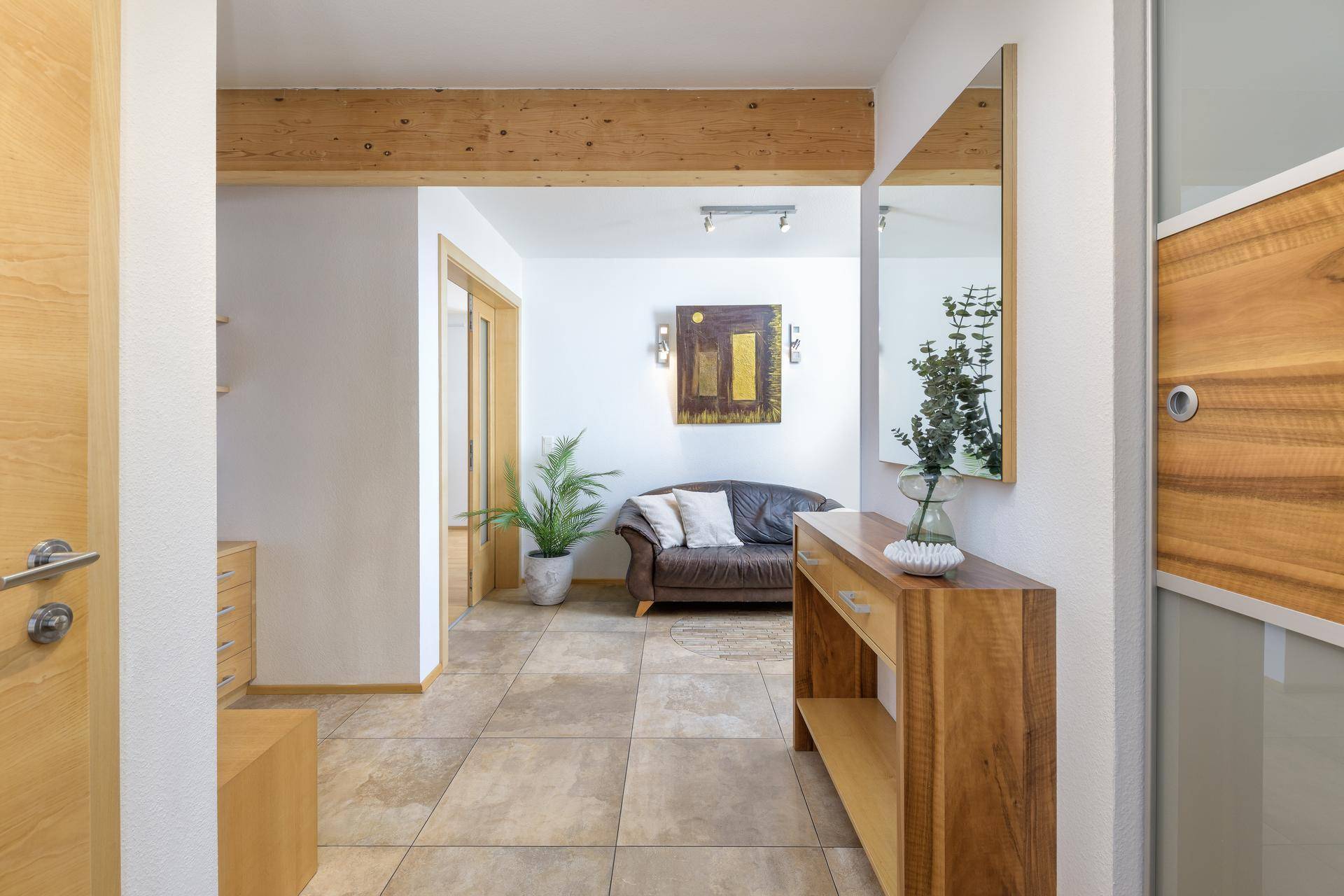 Heller Eingangsbereich mit Fliesenboden, Holzmöbeln und großem Spiegel.