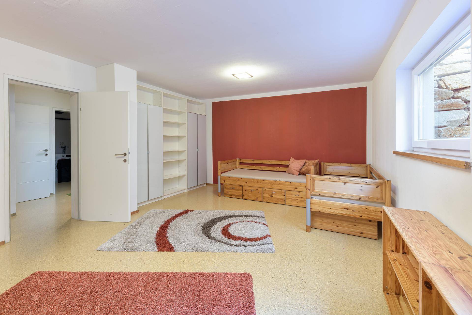 Ausgebauter Kellerraum mit Schlafsofa, roter Wand und Teppichen.