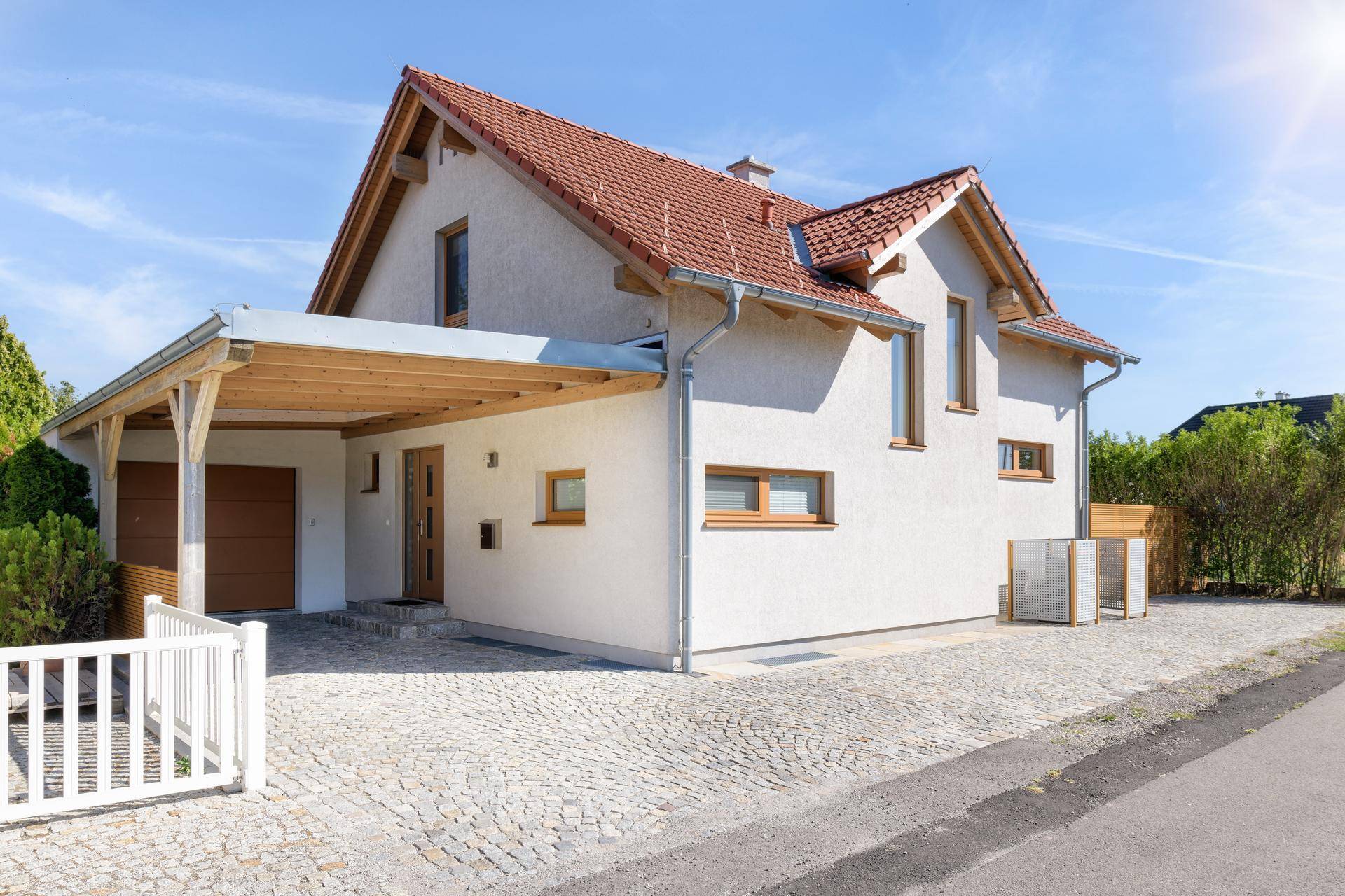 Modernes Einfamilienhaus mit Satteldach, Carport und gepflasterter Auffahrt.