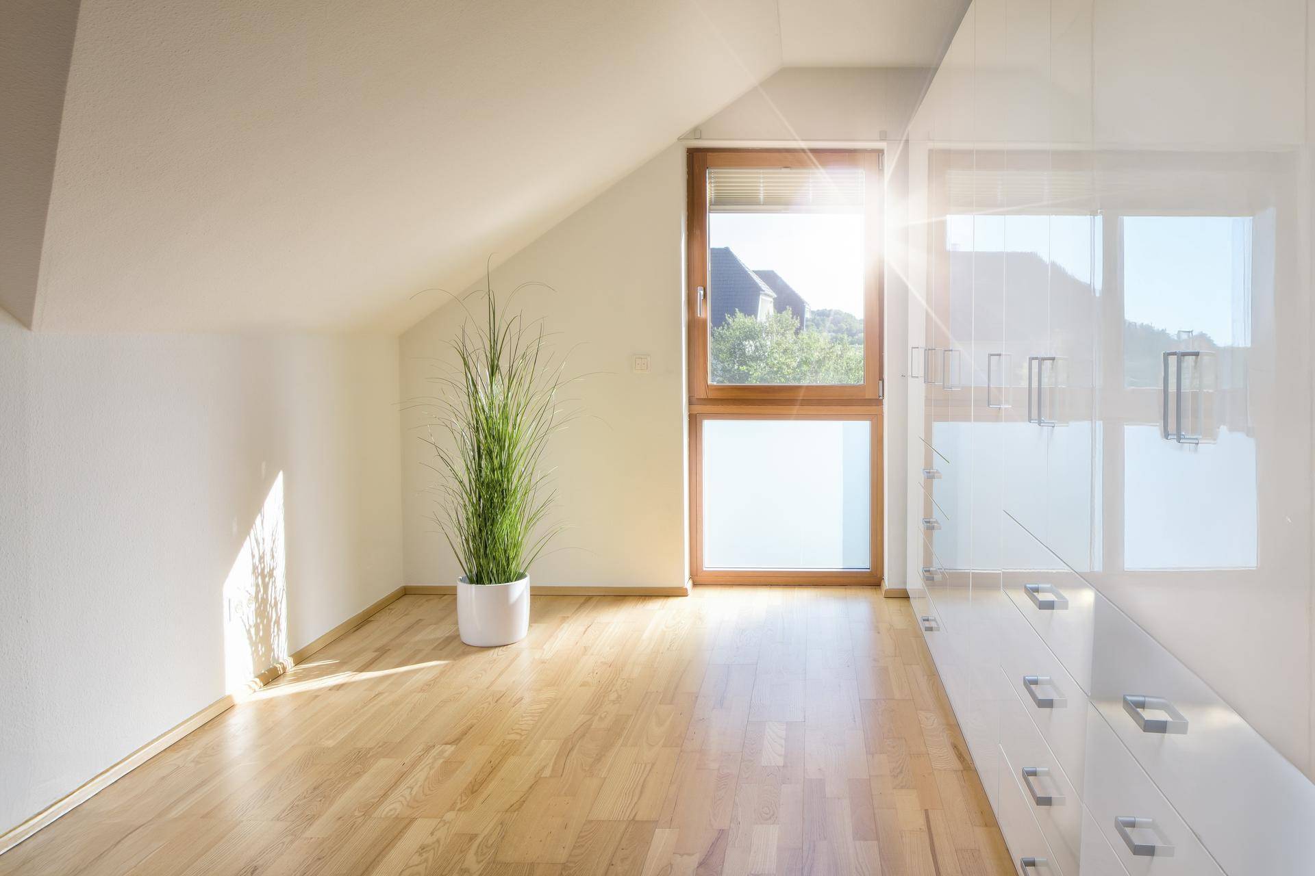 Lichtdurchflutetes Zimmer im Dachgeschoss mit Holzboden und großem Fenster.