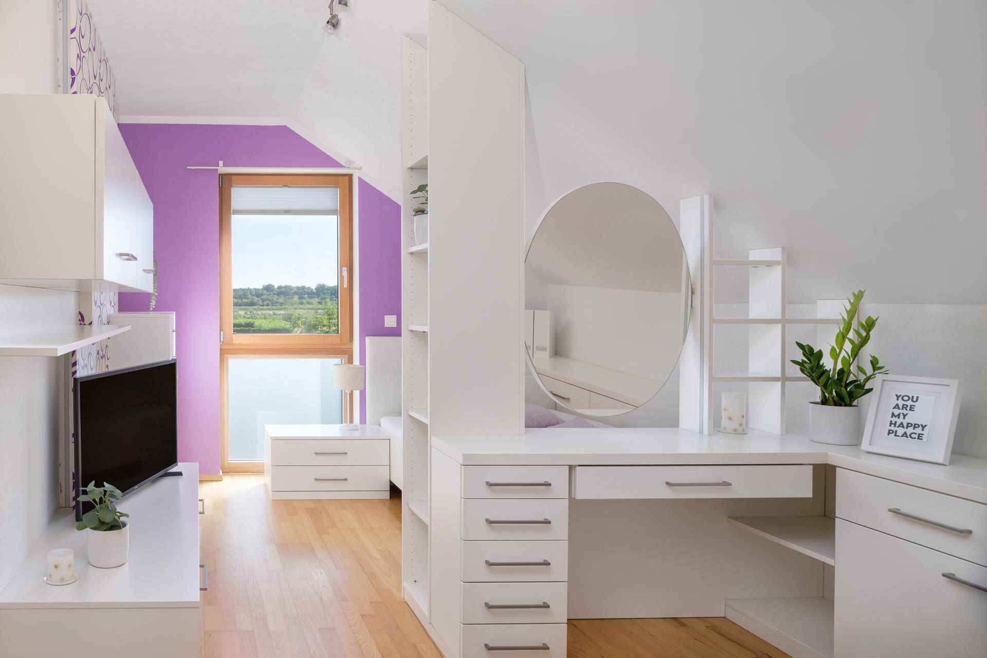 Farbiges Kinderzimmer im Dachgeschoss mit lila Wand, Schreibtisch und Spiegel.