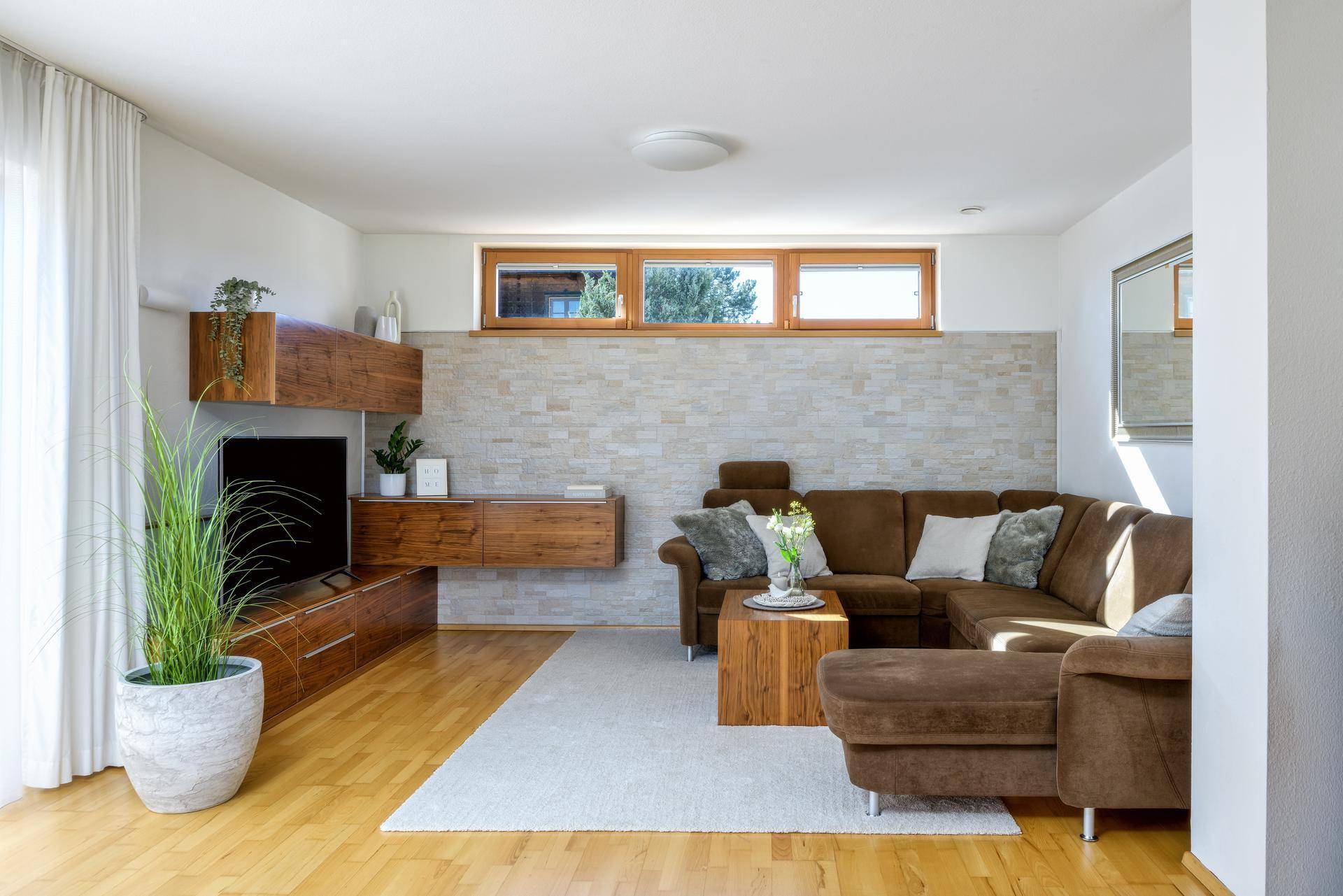 Gemütliches Wohnzimmer mit braunem Ecksofa, Holzelementen und Steinwandakzent.