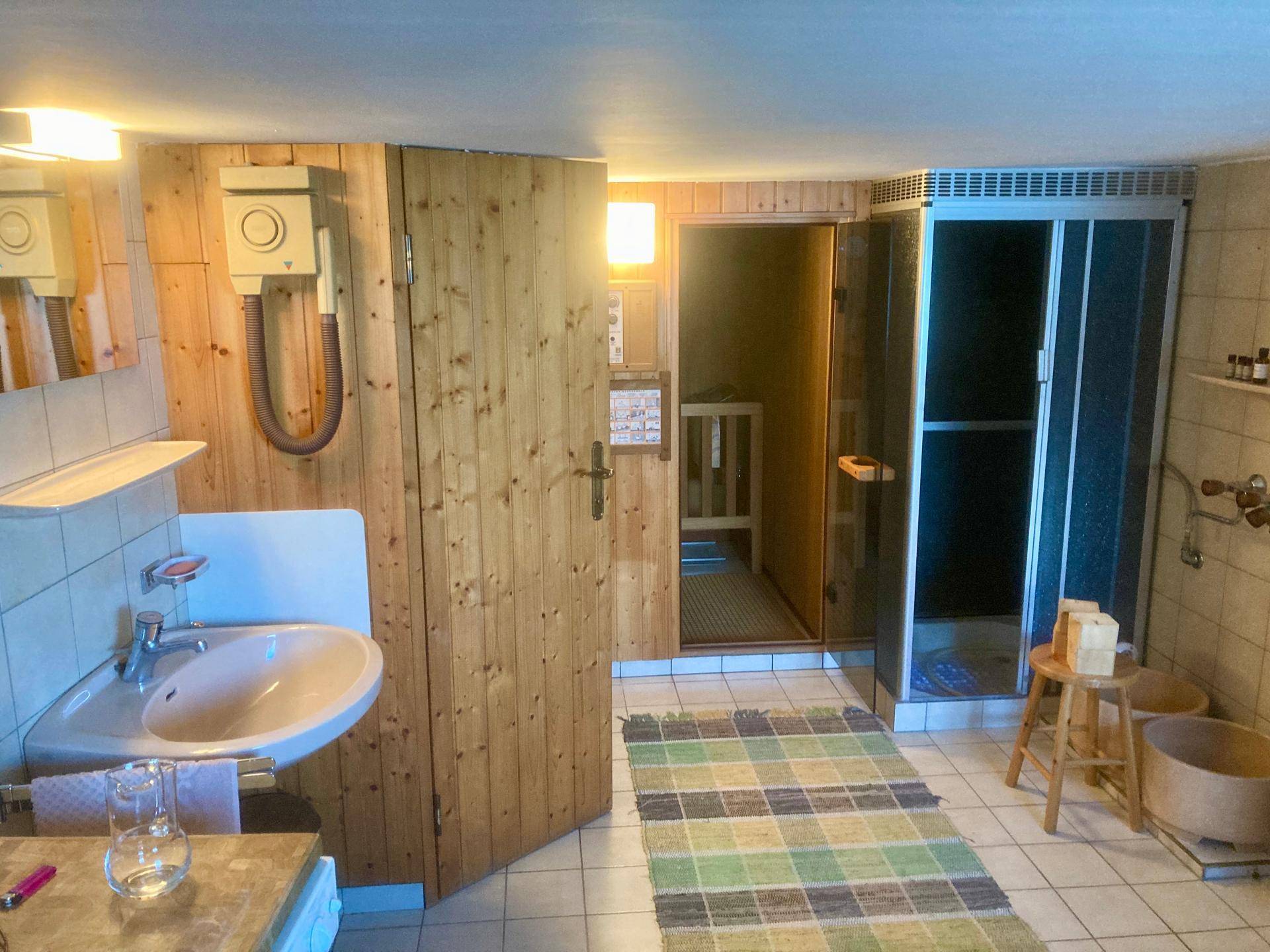 Badezimmer mit Sauna, Dusche und Holzverkleidung, im älteren Stil gehalten.