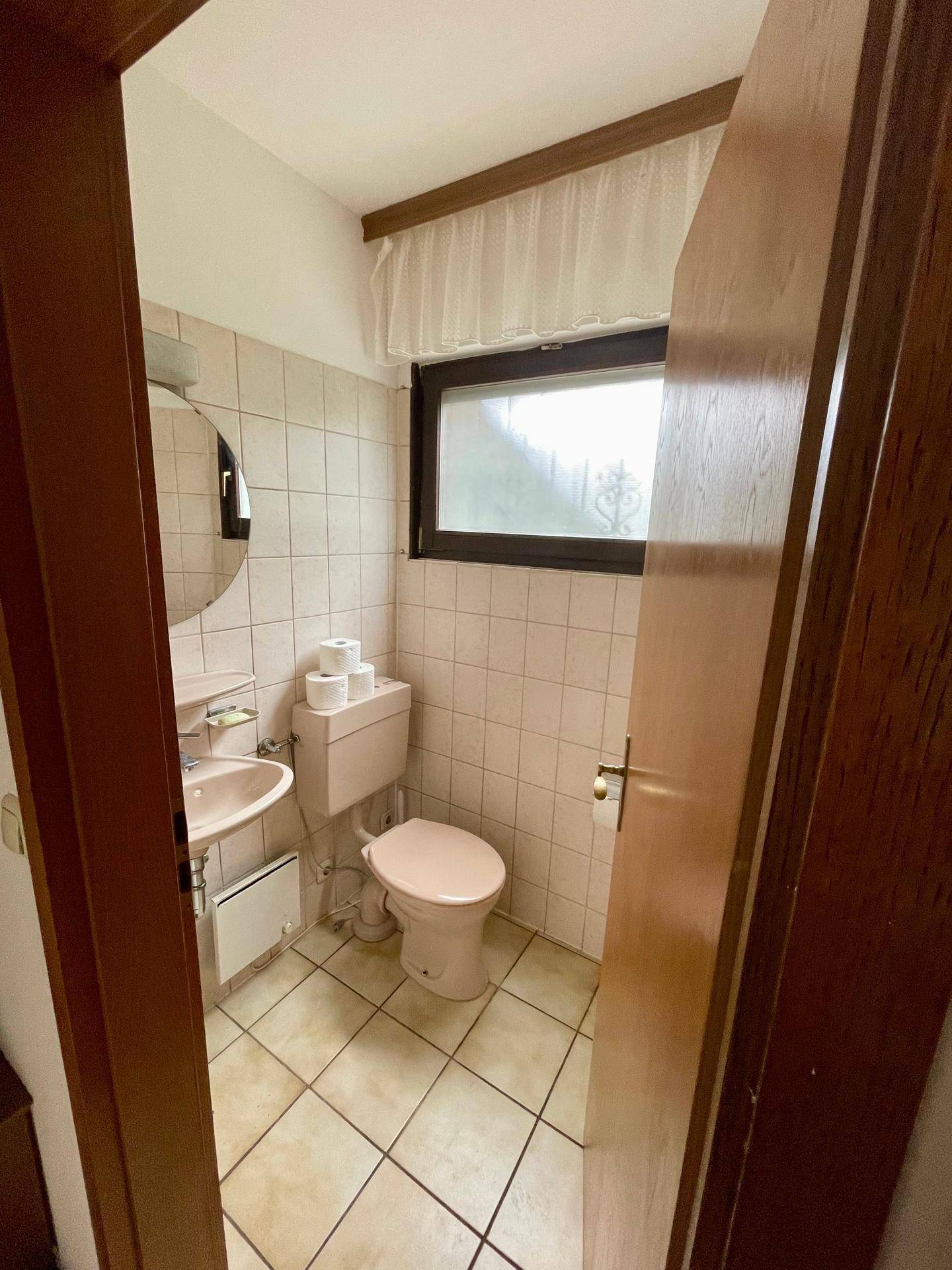 Kleines Gäste-WC mit rosa Sanitärobjekten, Fliesenboden und Fenster.