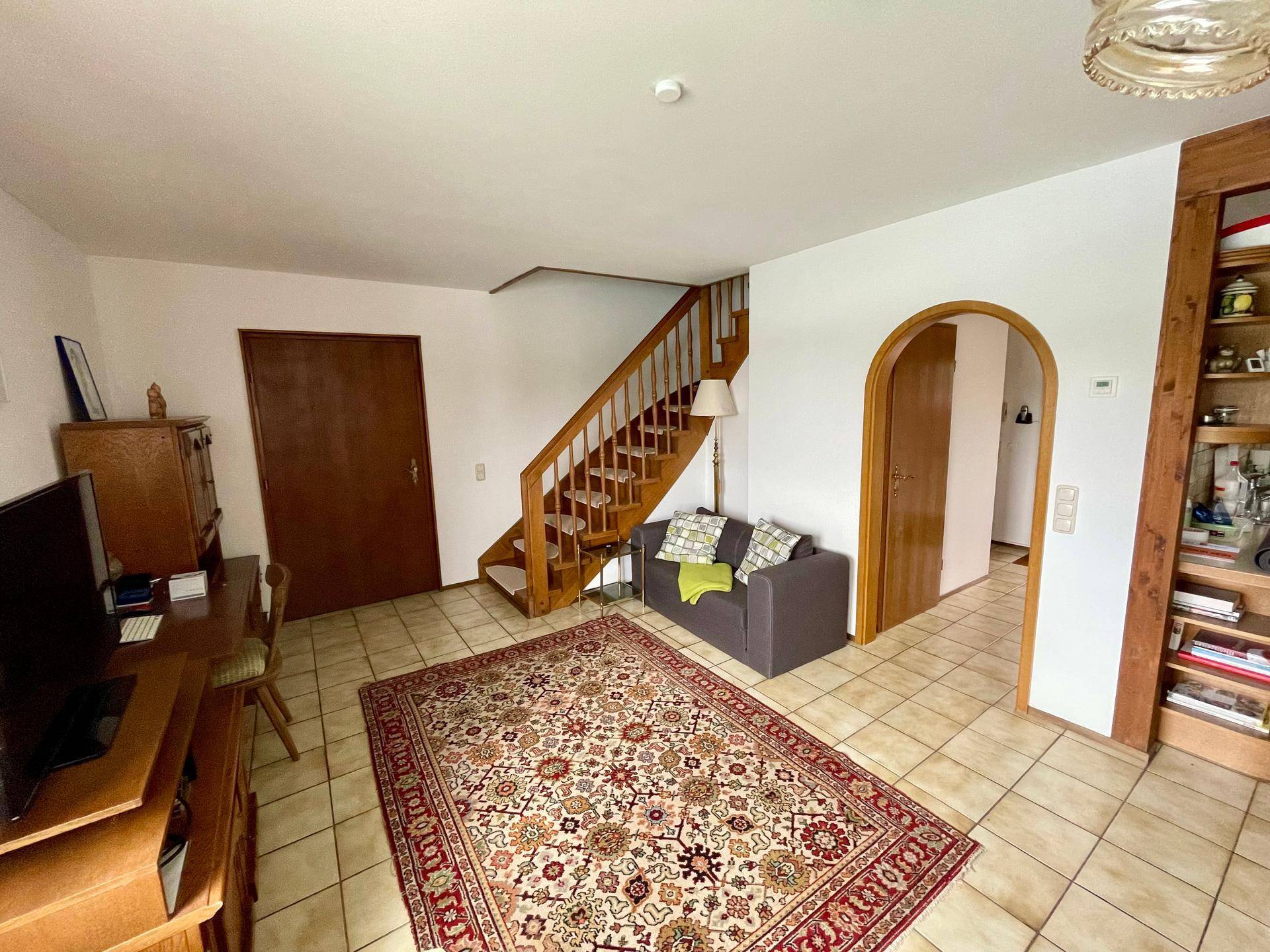 Geräumiges Wohnzimmer mit Holztreppe, Teppich und traditioneller Einrichtung.