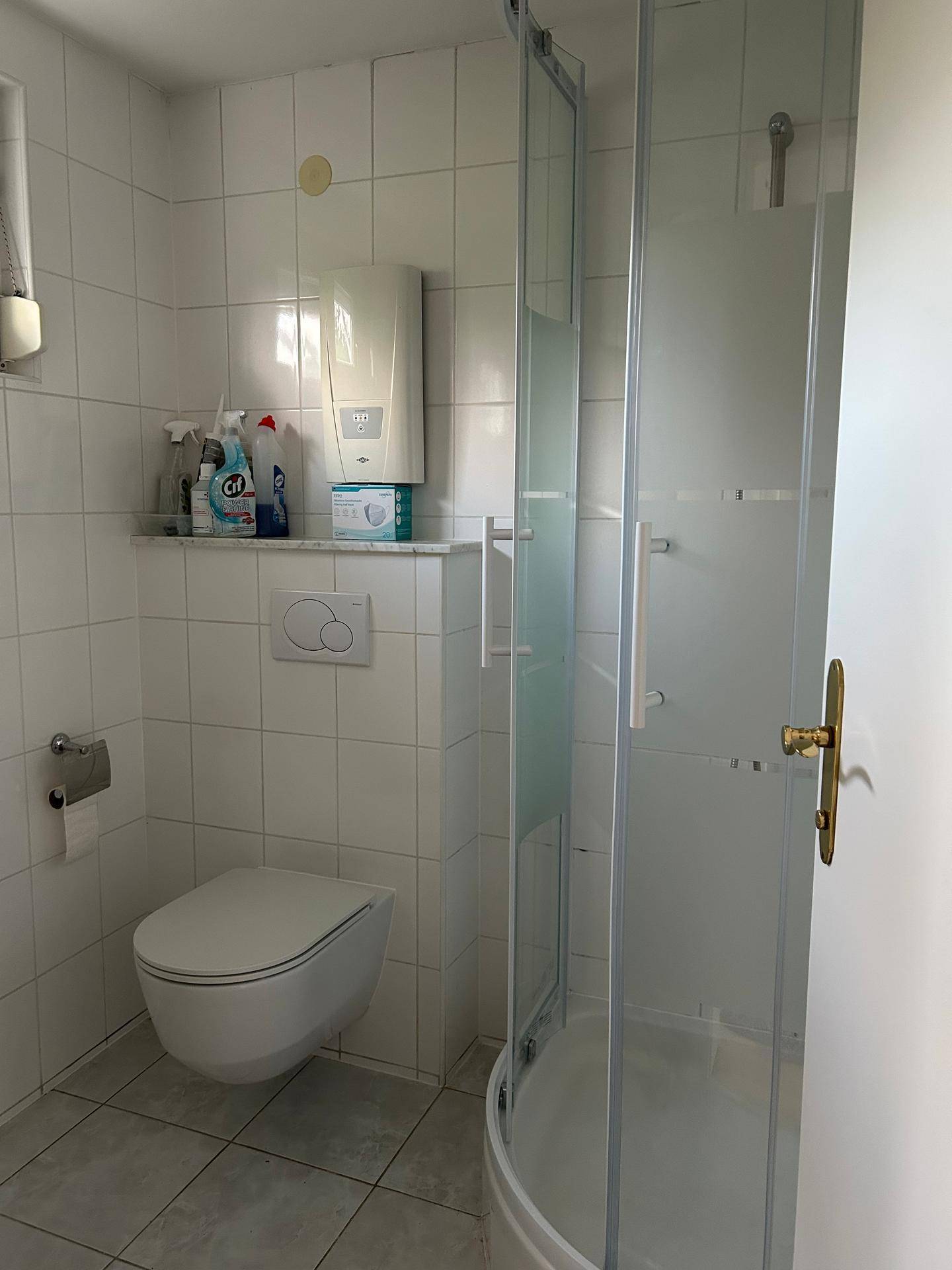 Modernes Badezimmer mit weißen Fliesen, wandhängendem WC und einer Duschkabine in der Ecke.