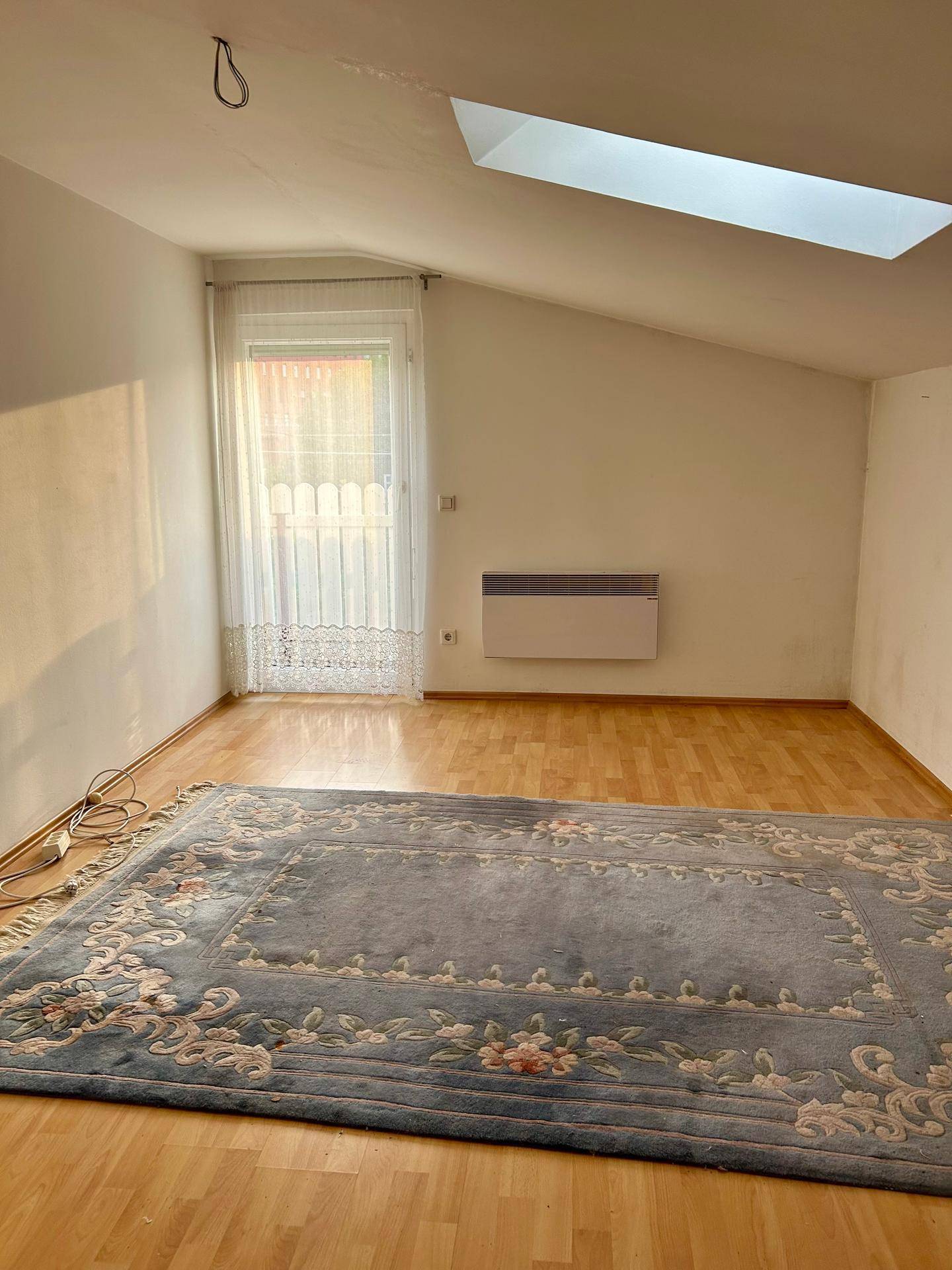 Helles Schlafzimmer mit Dachschräge, Holzboden, Heizkörper und einem Dachfenster für viel Licht.