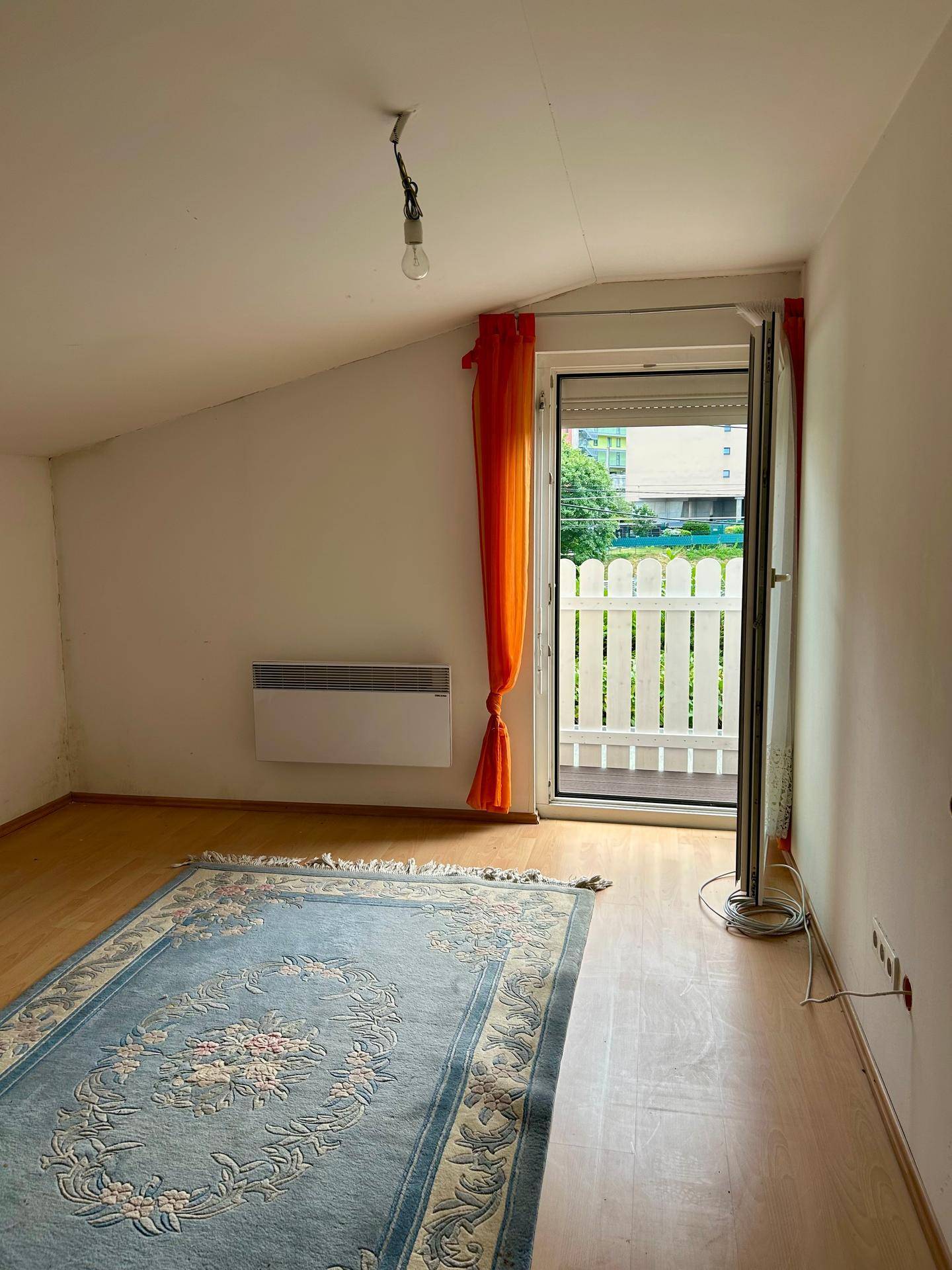 Schlafzimmer mit Dachschräge, Holzboden und Zugang zu einem kleinen Balkon mit weißem Zaun.