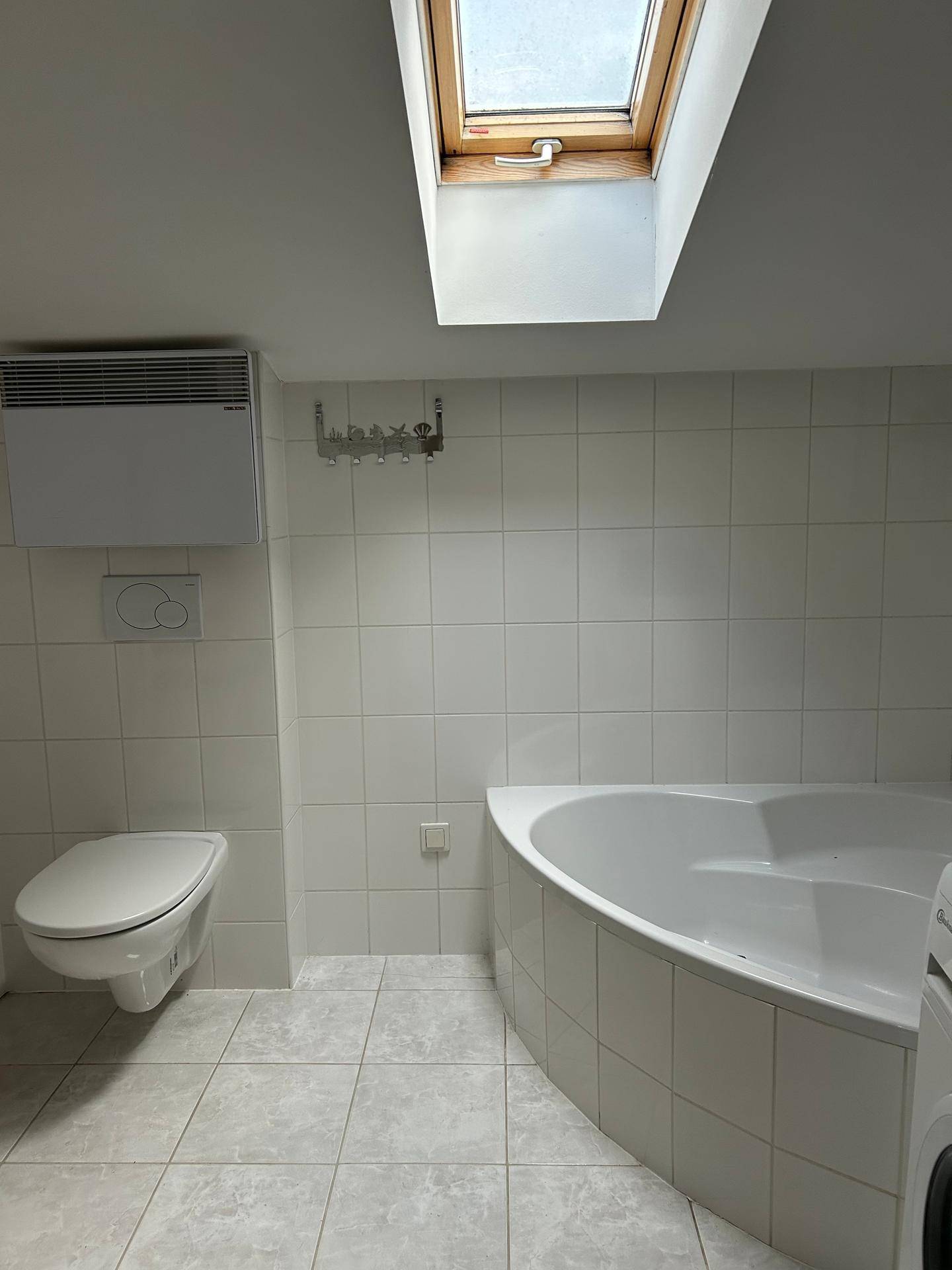 Helles Badezimmer mit weißen Fliesen, Eckbadewanne, wandhängendem WC und einem Dachfenster.
