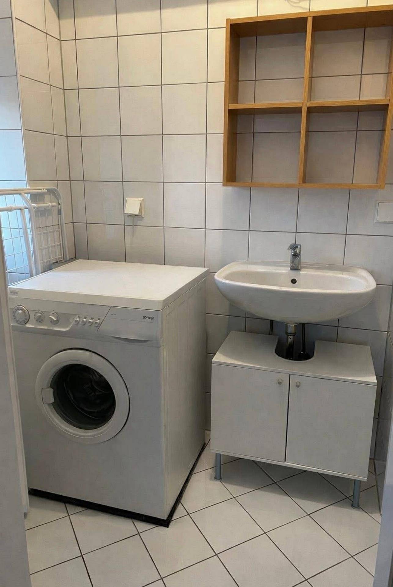 Badezimmer mit Waschmaschine, Waschbecken und weißen Fliesen an Wänden und Boden.