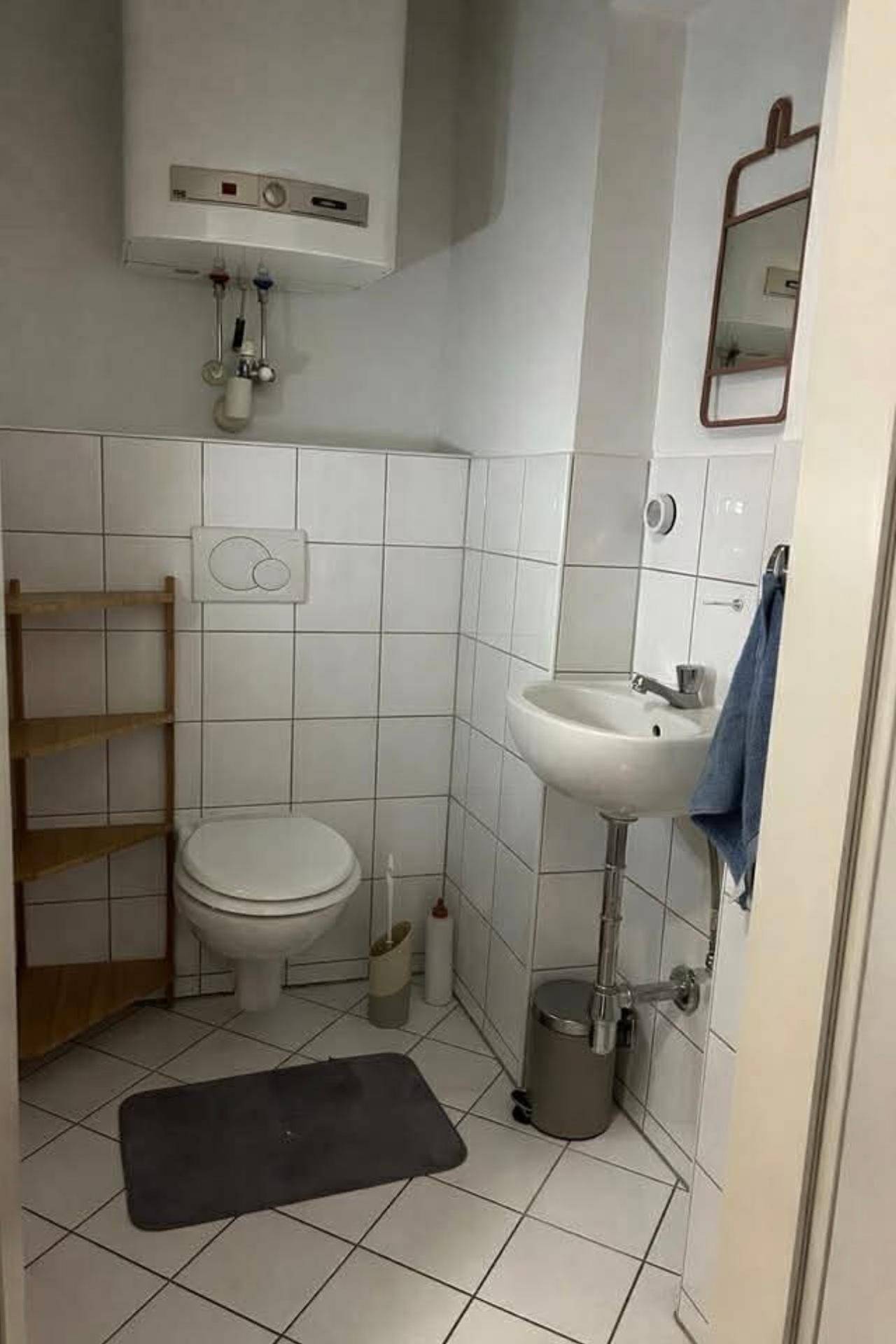 Kleines WC mit wandhängender Toilette, Waschbecken und Boiler an der Wand.