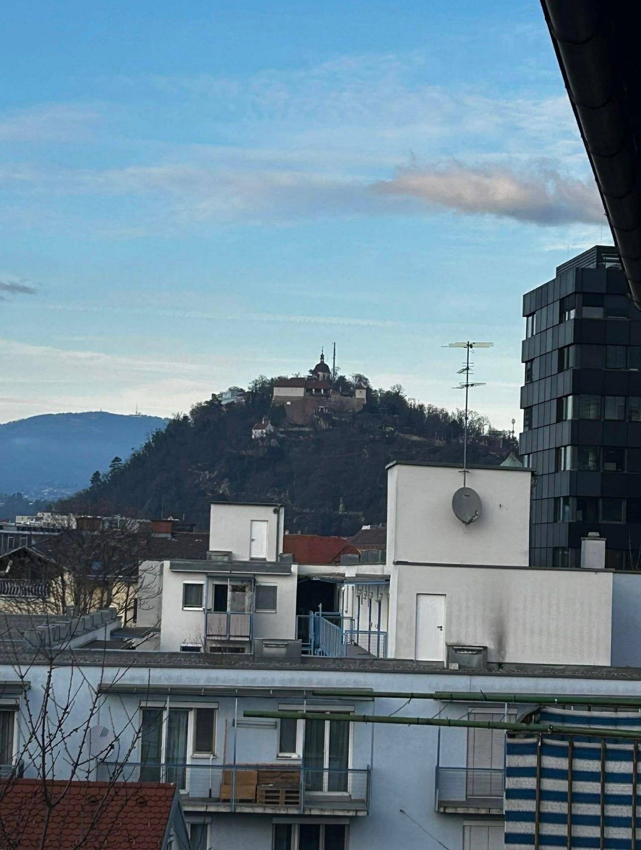 Panoramablick über die Stadt mit einem Hügel und historischen Gebäuden im Hintergrund.