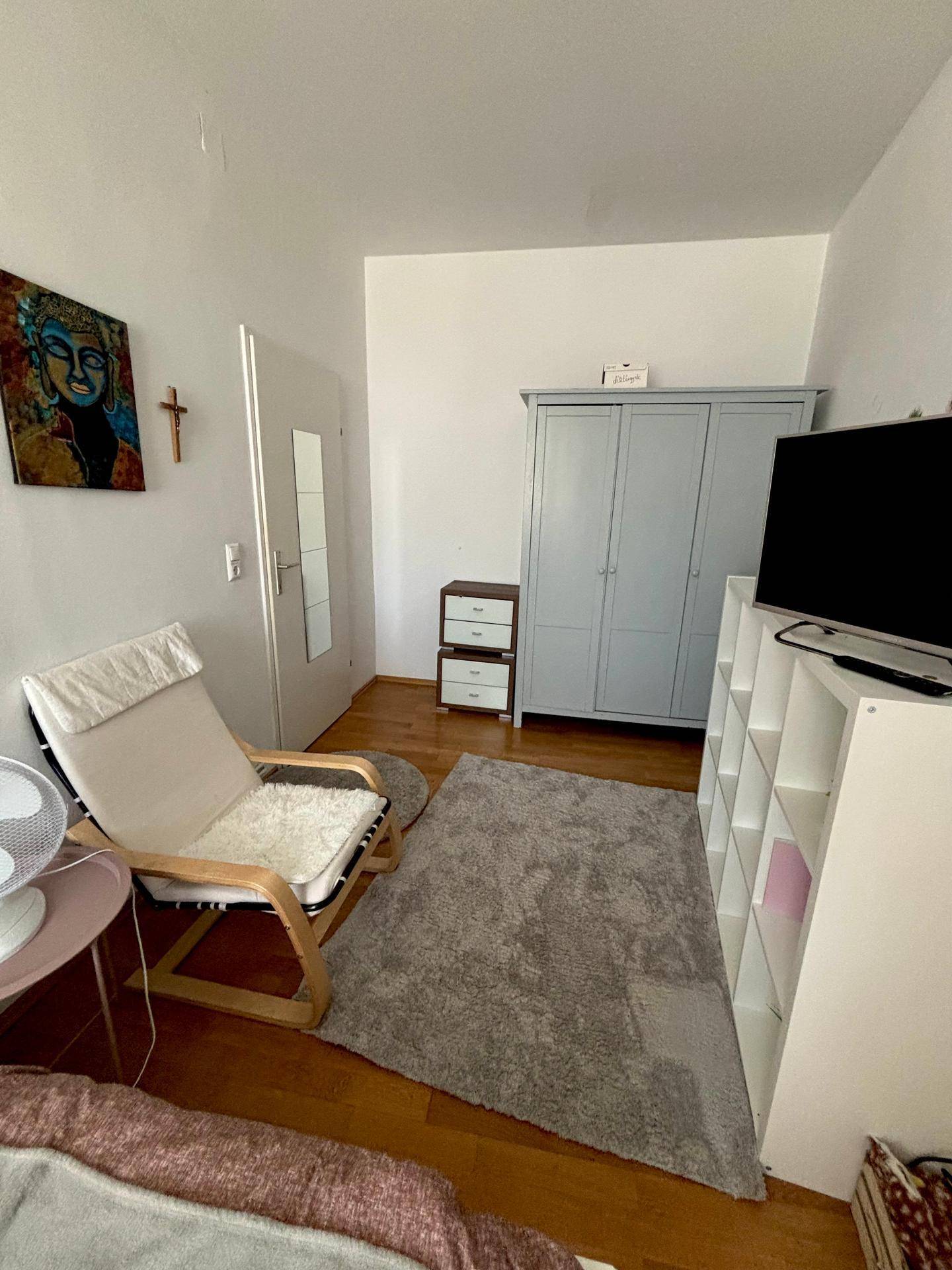 Schlafzimmer mit hellem Holzboden, grauem Kleiderschrank und einem gemütlichen Sessel.