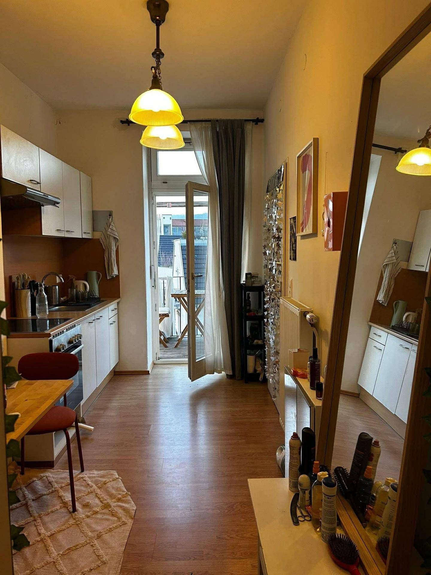 Schmale Küche mit weißer Einbauküche, Holzboden und Zugang zu einem kleinen Balkon.