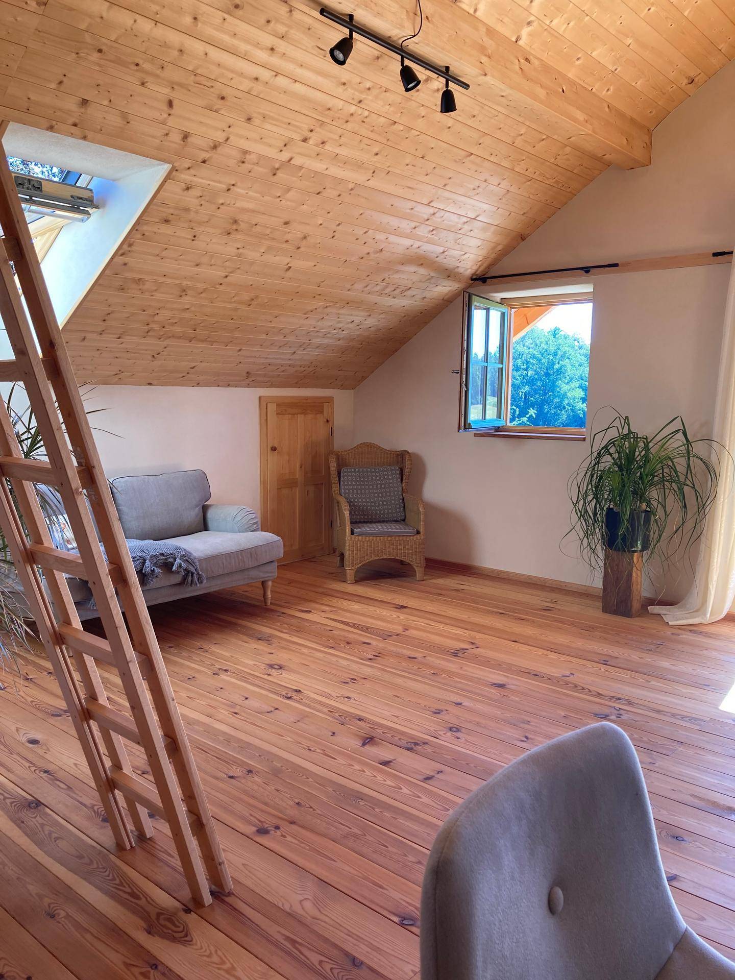 Geräumiger Wohnbereich mit Holzboden, Dachschrägen und Blick ins Grüne.