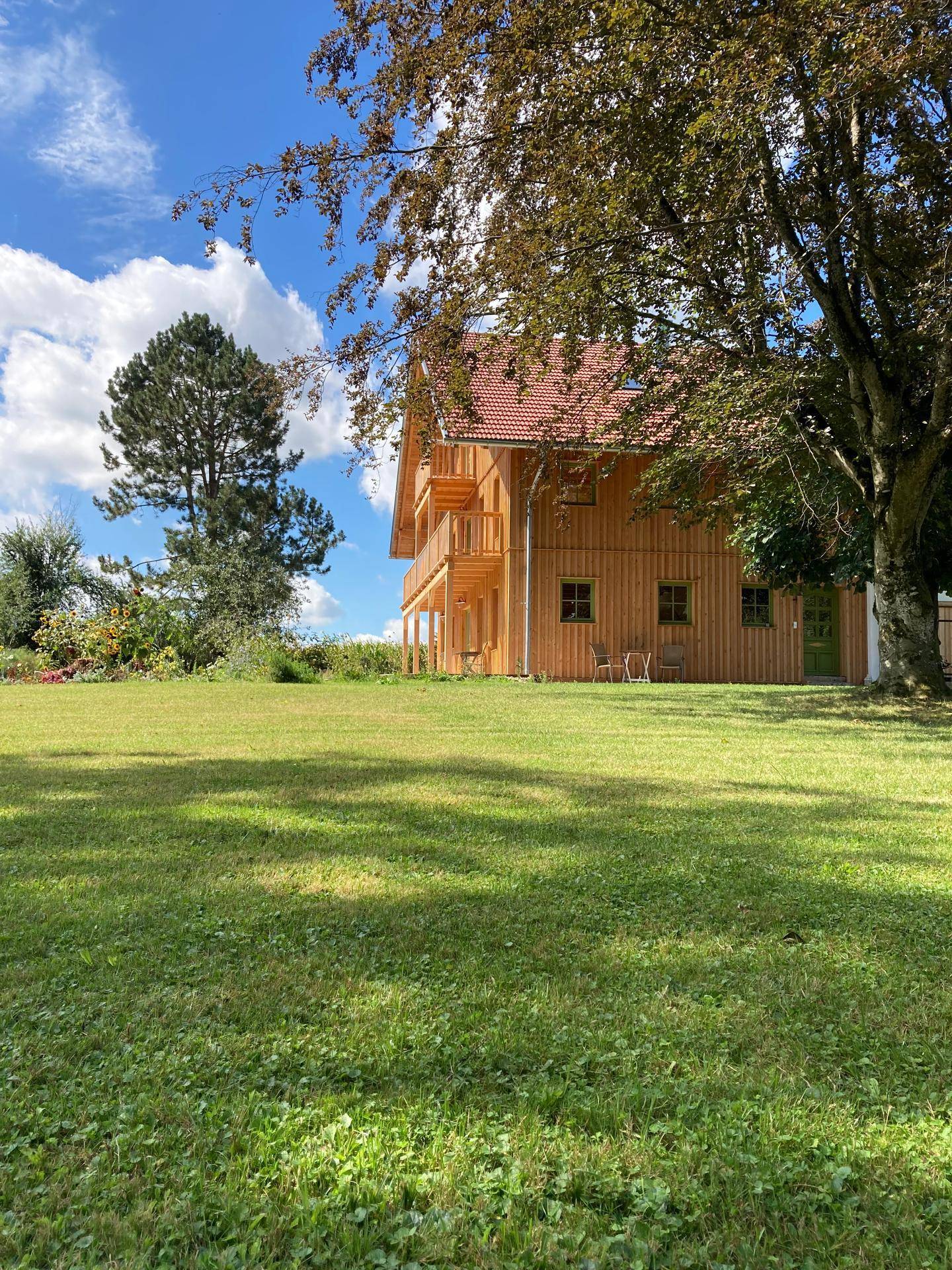 Charmantes Holzhaus mit Balkonen und großem Garten, umgeben von Bäumen und Natur.