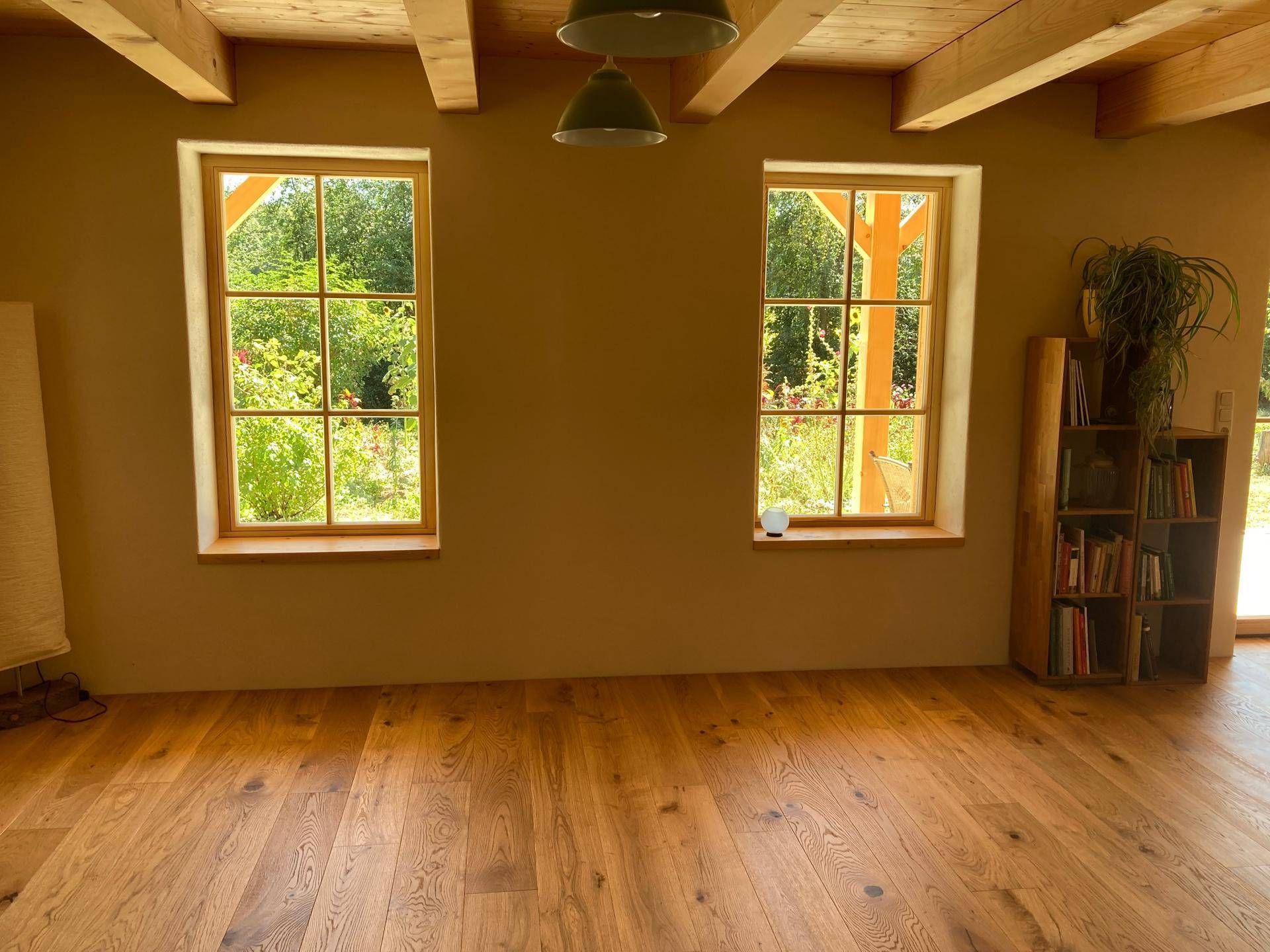 Heller Wohnraum mit Holzboden, großen Fenstern und Blick auf die grüne Umgebung.