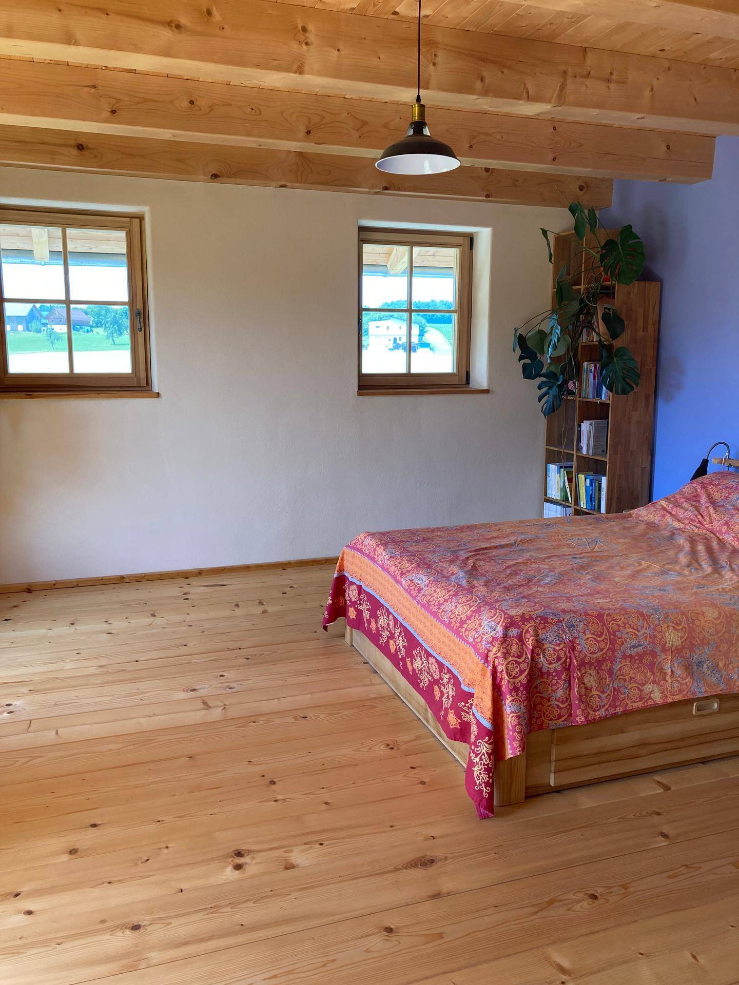 Schlafzimmer mit Holzdielenboden, Bett und Fenstern mit Blick auf die Landschaft.