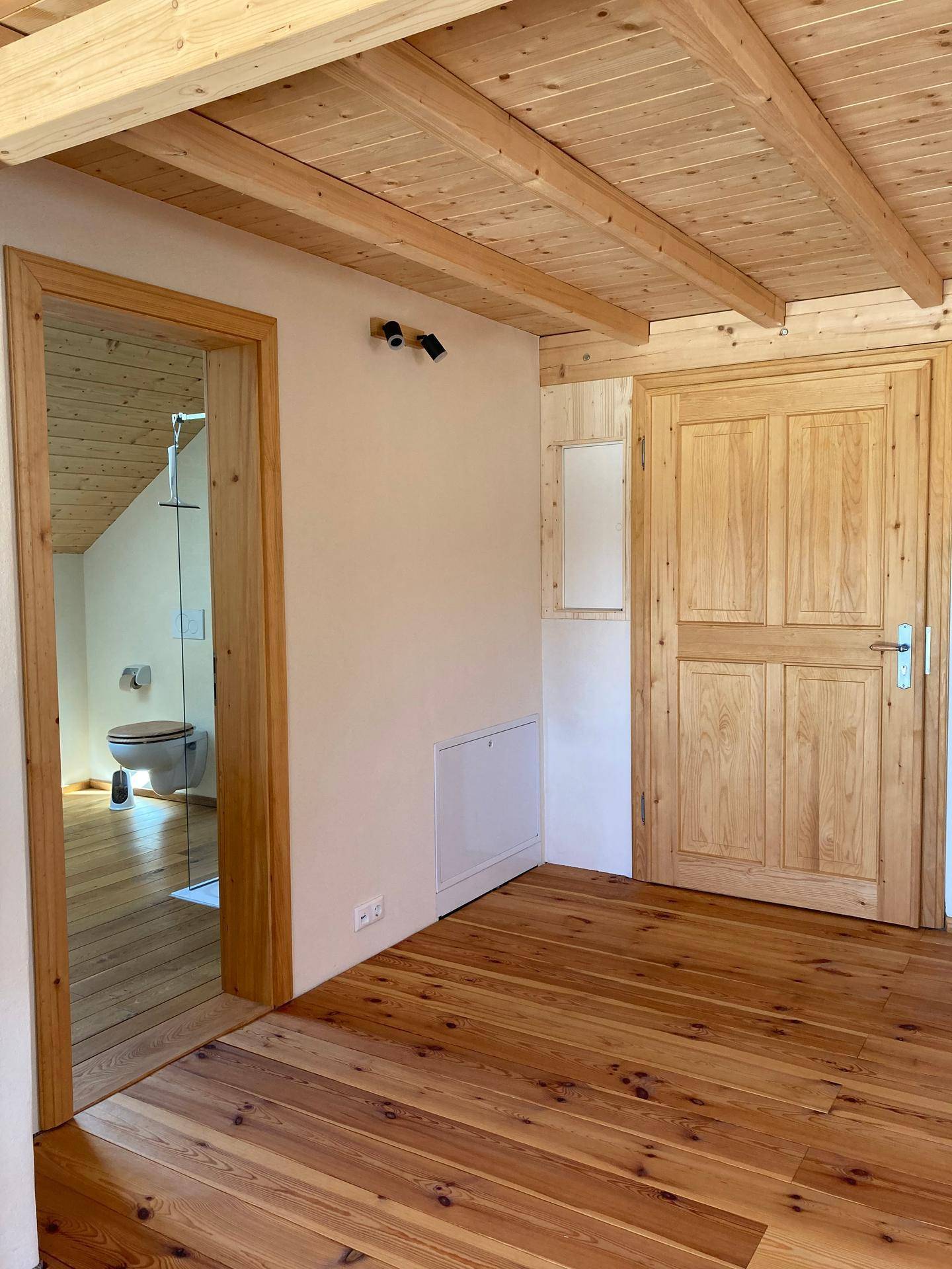 Heller Flur mit Holzboden und Holztüren, eine führt zu einem angrenzenden Badezimmer.