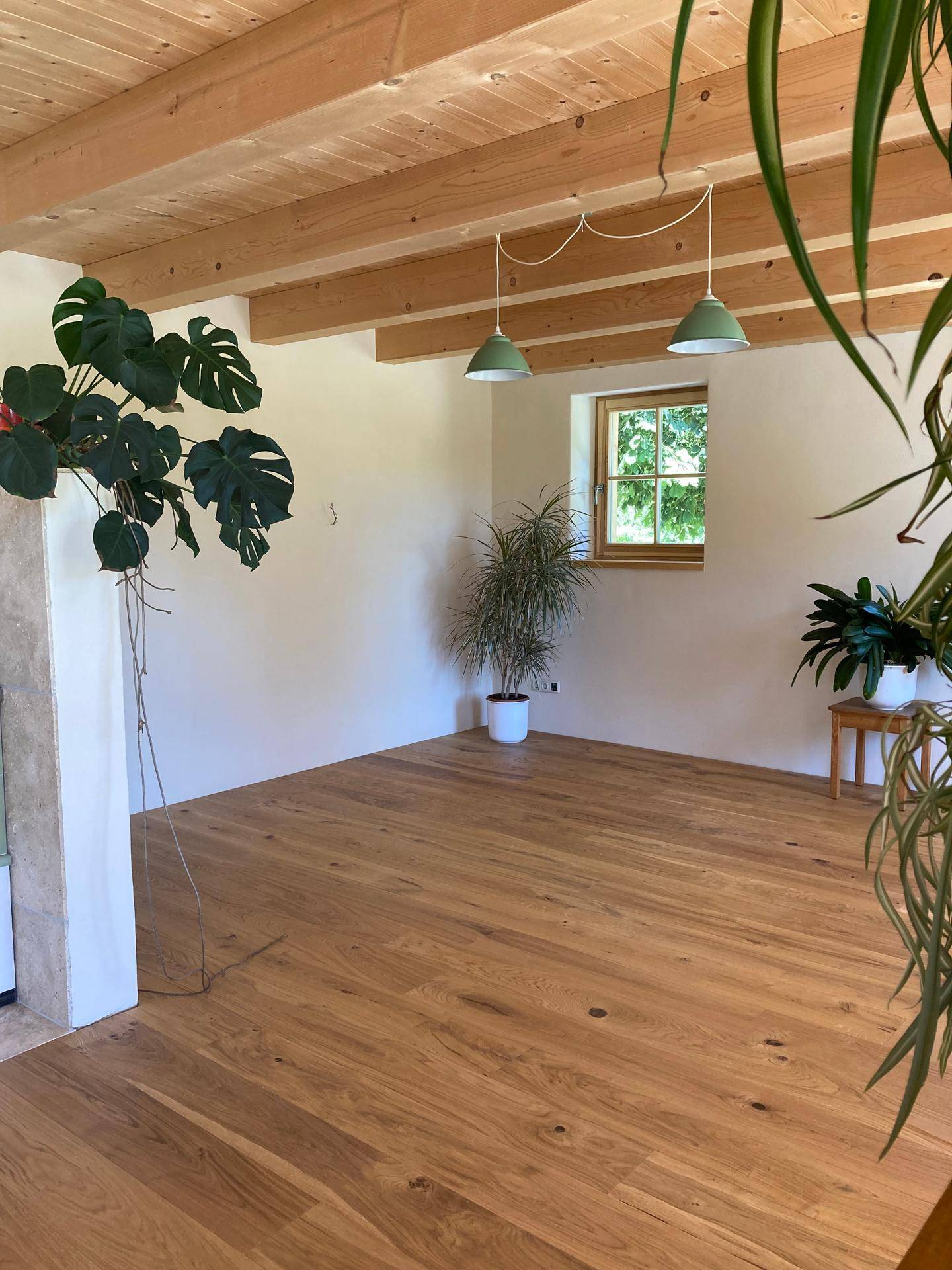 Geräumiger, heller Wohnbereich mit Holzboden und sichtbaren Deckenbalken.