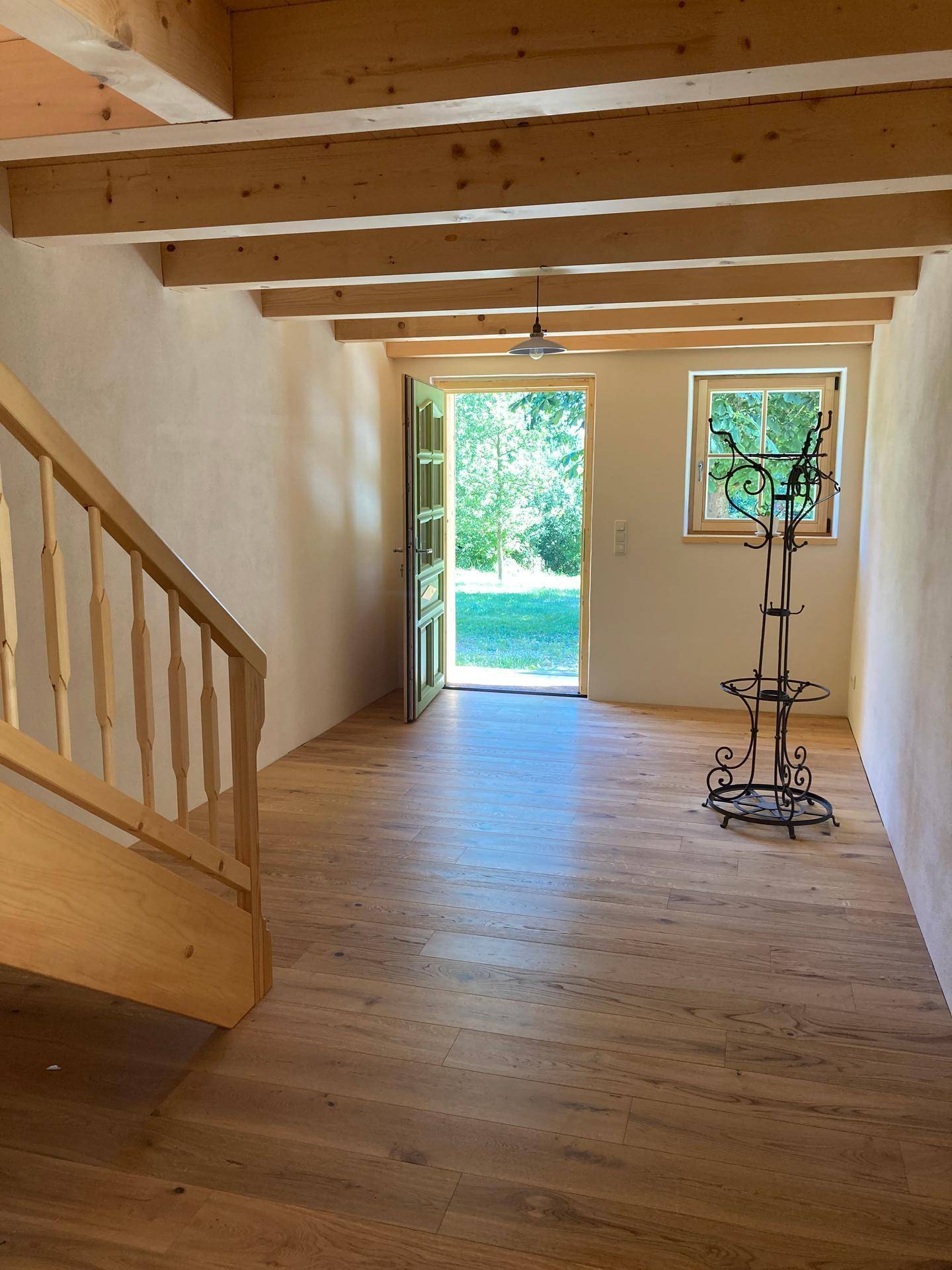 Heller Eingangsbereich mit Holztreppe, Holzboden und Blick ins Grüne durch die offene Tür.