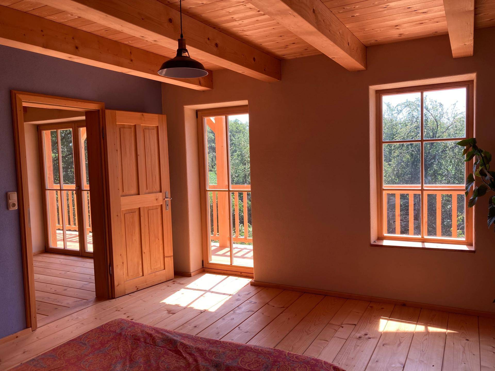 Schlafzimmer mit Holzdielenboden, Holztüren und Zugang zu einem weiteren Raum oder Balkon.