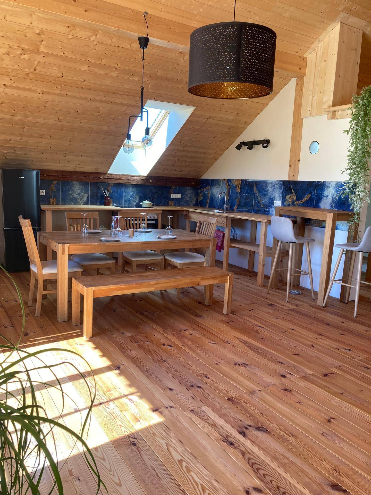 Offener Wohn- und Essbereich mit Holzboden, Dachschräge, Essbereich und einer Küchenzeile mit blauen Fliesen.