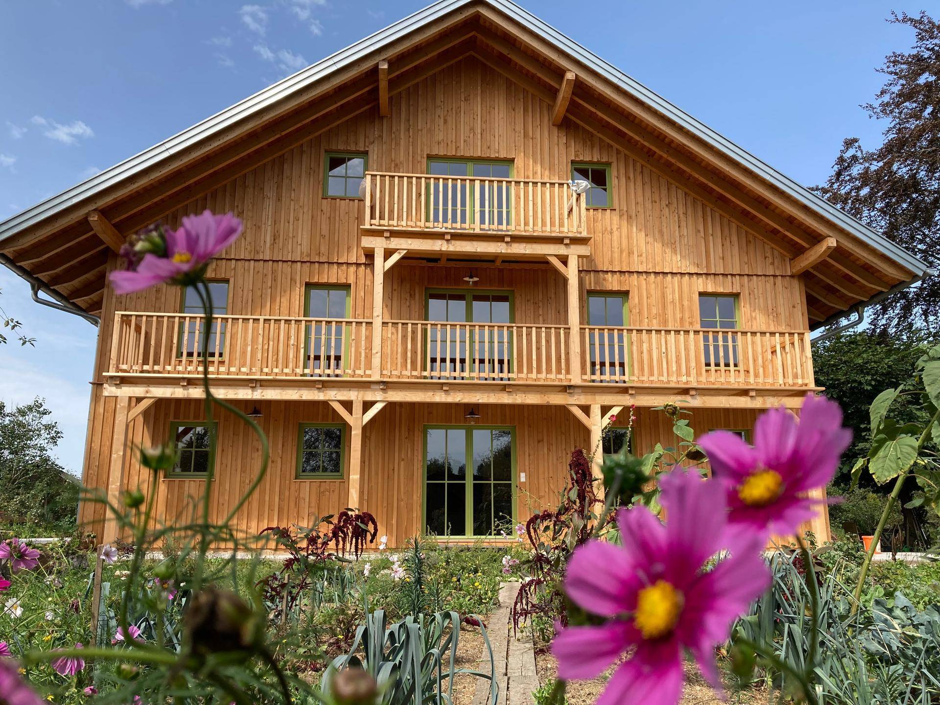 Rosa Blüten im Vordergrund vor der Holzfassade des Hauses mit seinen charmanten Balkonen.