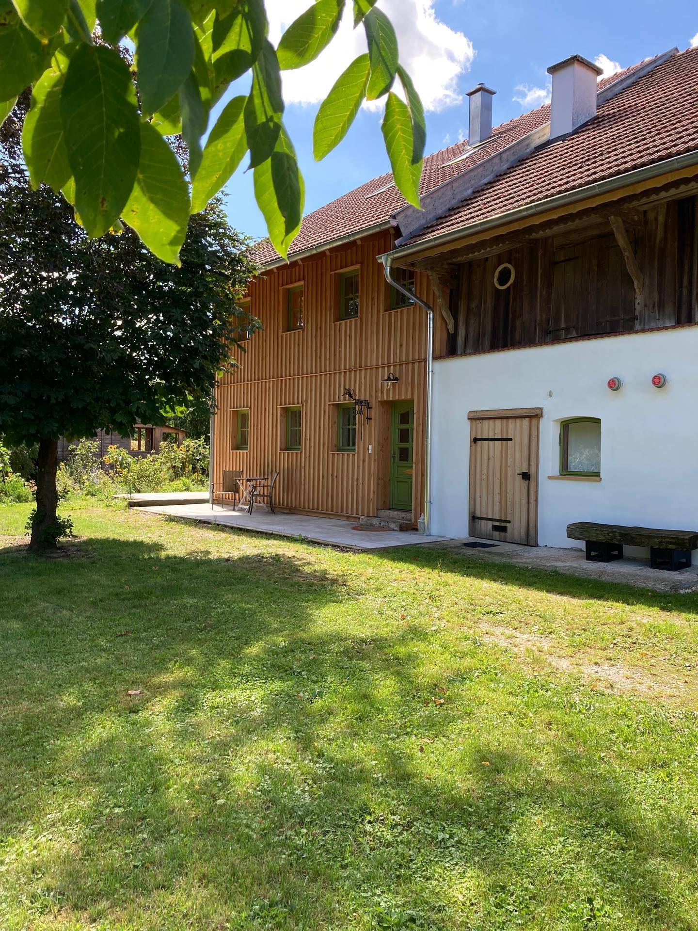 Seitenansicht des Holzhauses mit angrenzendem Gebäude und einem gepflegten Rasenbereich.