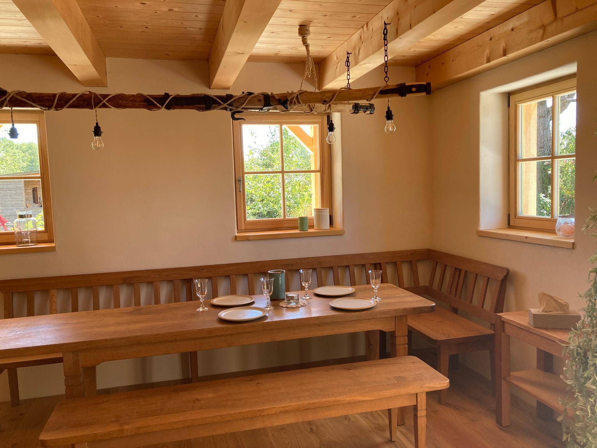 Heller Essbereich mit rustikalem Holztisch und Bänken unter einer Holzbalkendecke.