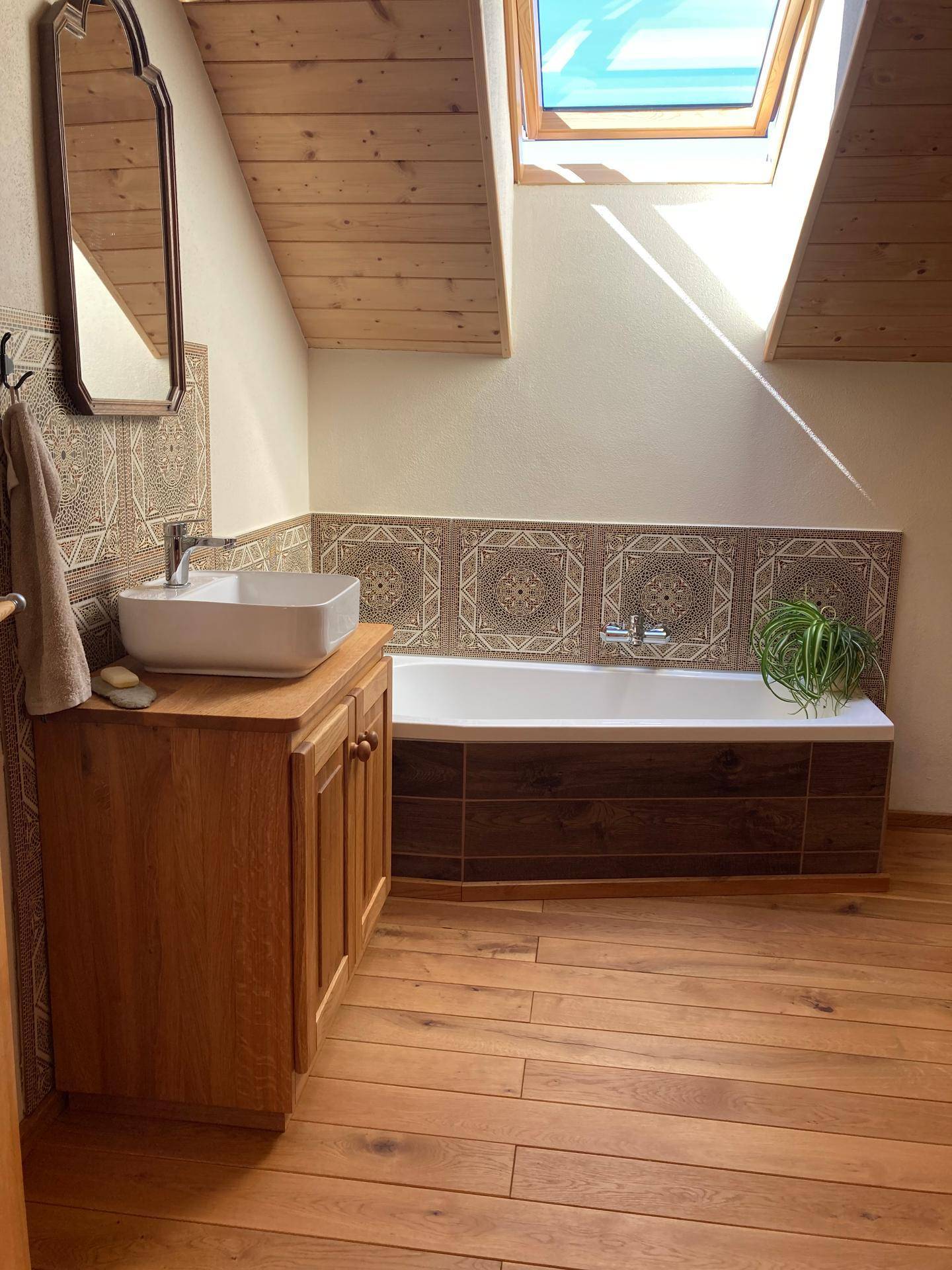 Helles Badezimmer mit Holzboden, Badewanne und Waschtisch unter Dachschräge.