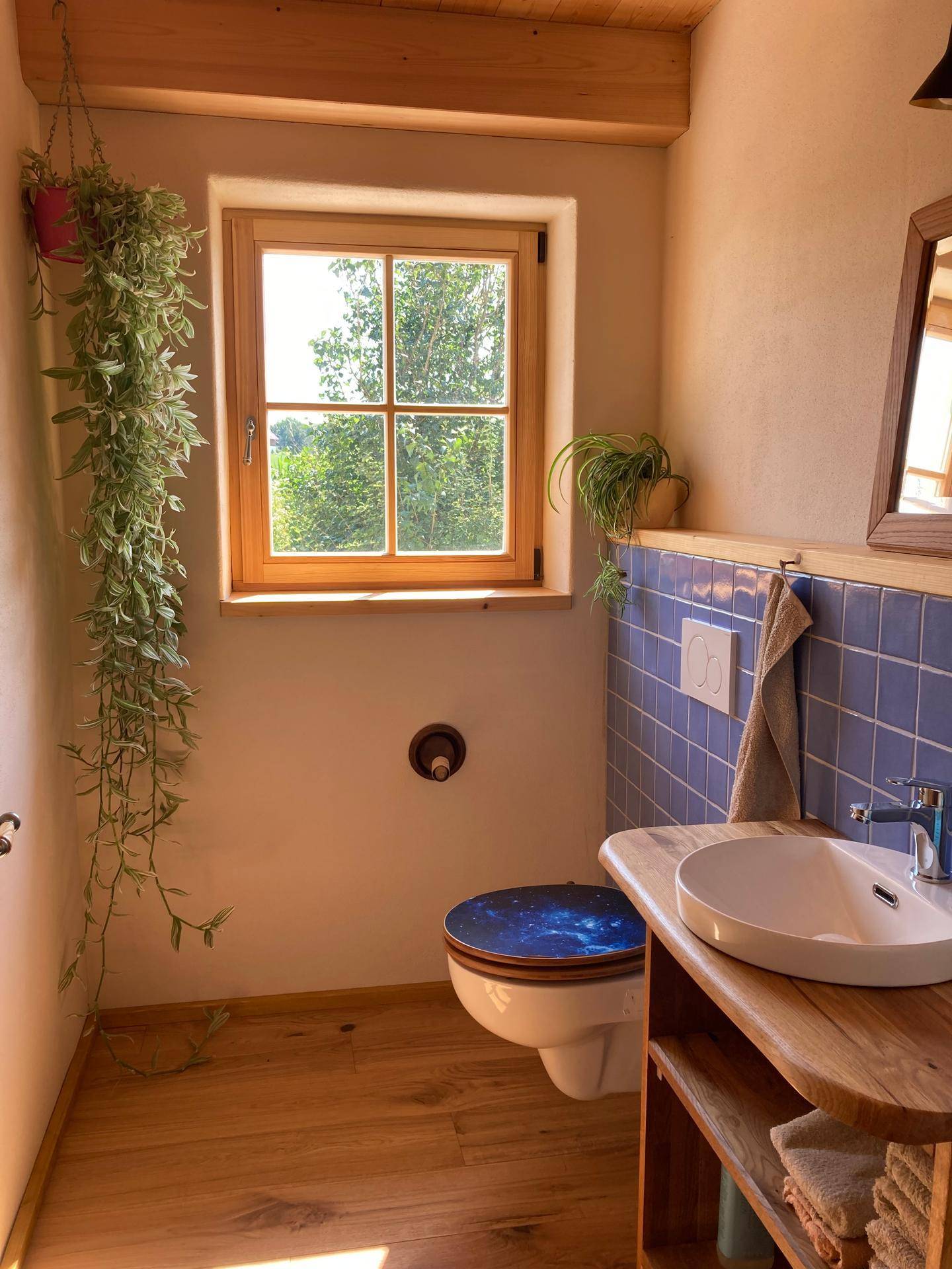 Freundliches Gäste-WC mit Holzwaschtisch, blauen Fliesen und Fenster.