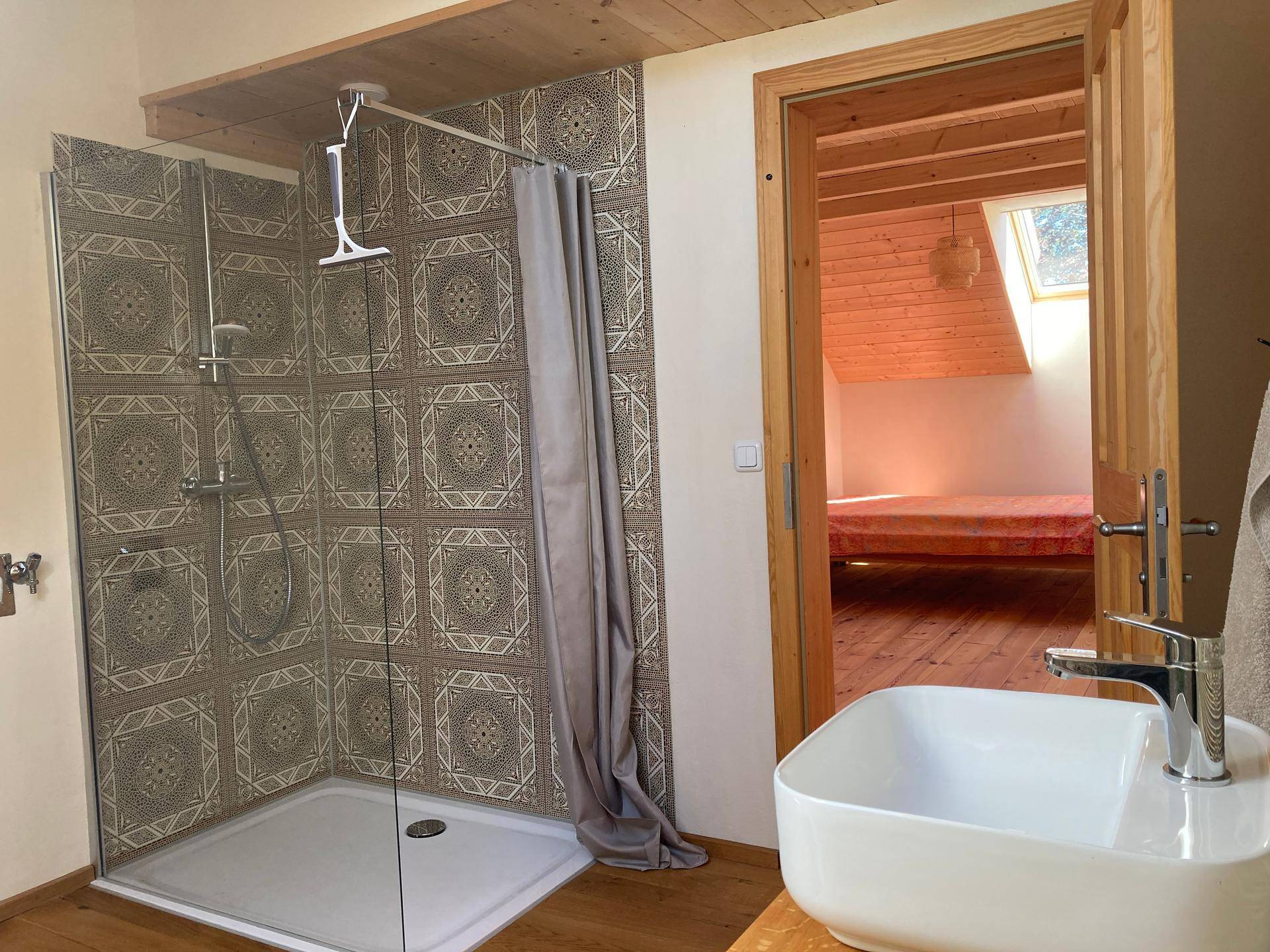 Badezimmer mit Dusche und Waschtisch, mit Zugang zu einem angrenzenden Schlafzimmer.